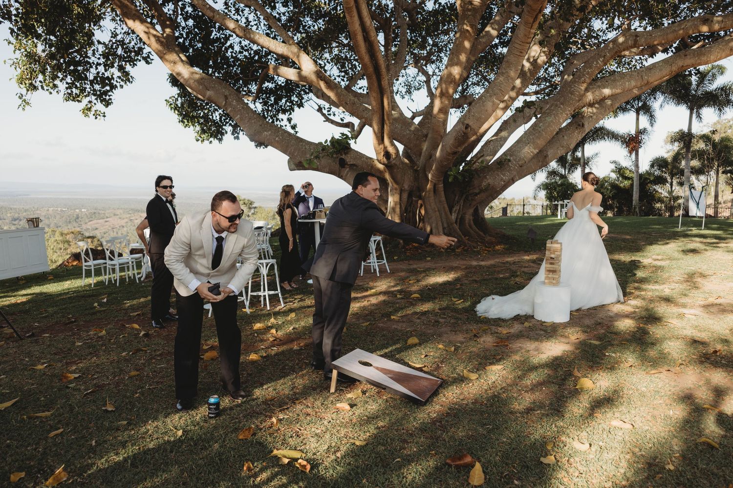 Wedding guests gathering under a large sprawling tree during an outdoor celebration.