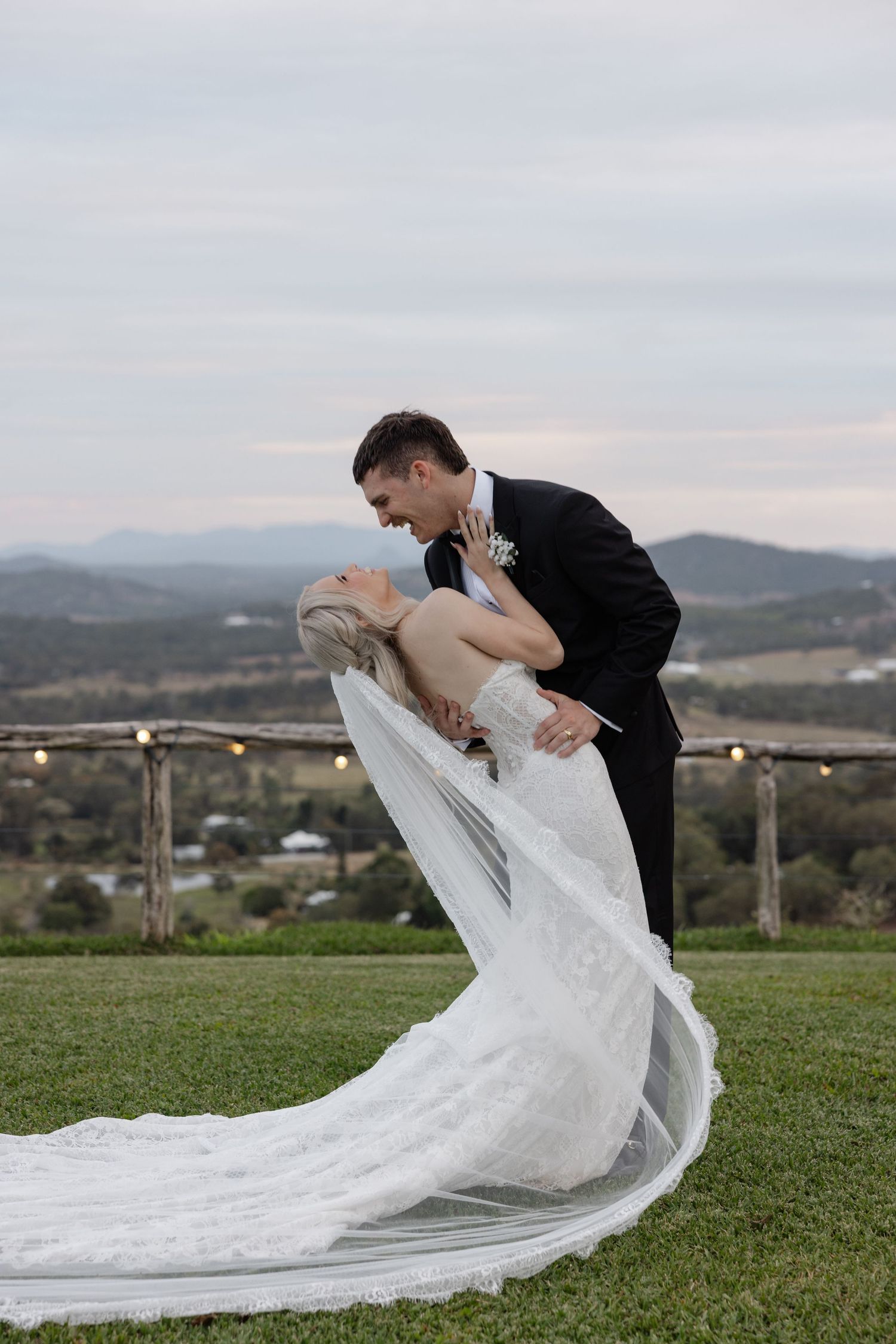A groom dips his bride in a romantic wedding pose with a flowing veil and scenic mountain backdrop.