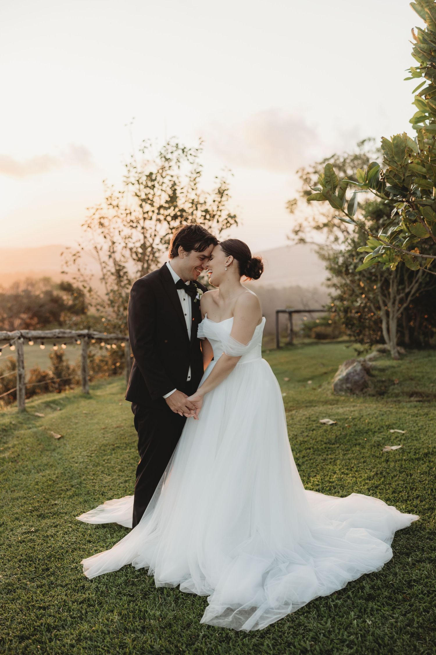 Romantic sunset wedding portraits on grassy hillside with mountain views.