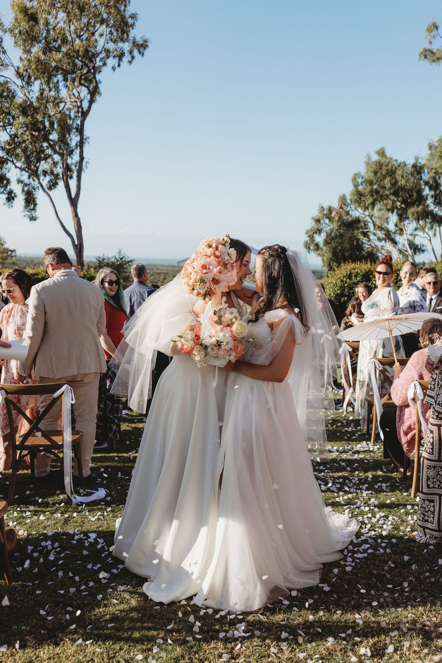 Wedding party celebrates with confetti in an outdoor garden setting with white dresses.