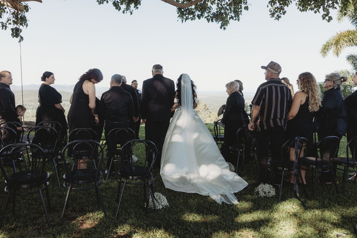 Wedding guests seated in rows of black chairs on a lawn during an outdoor ceremony.