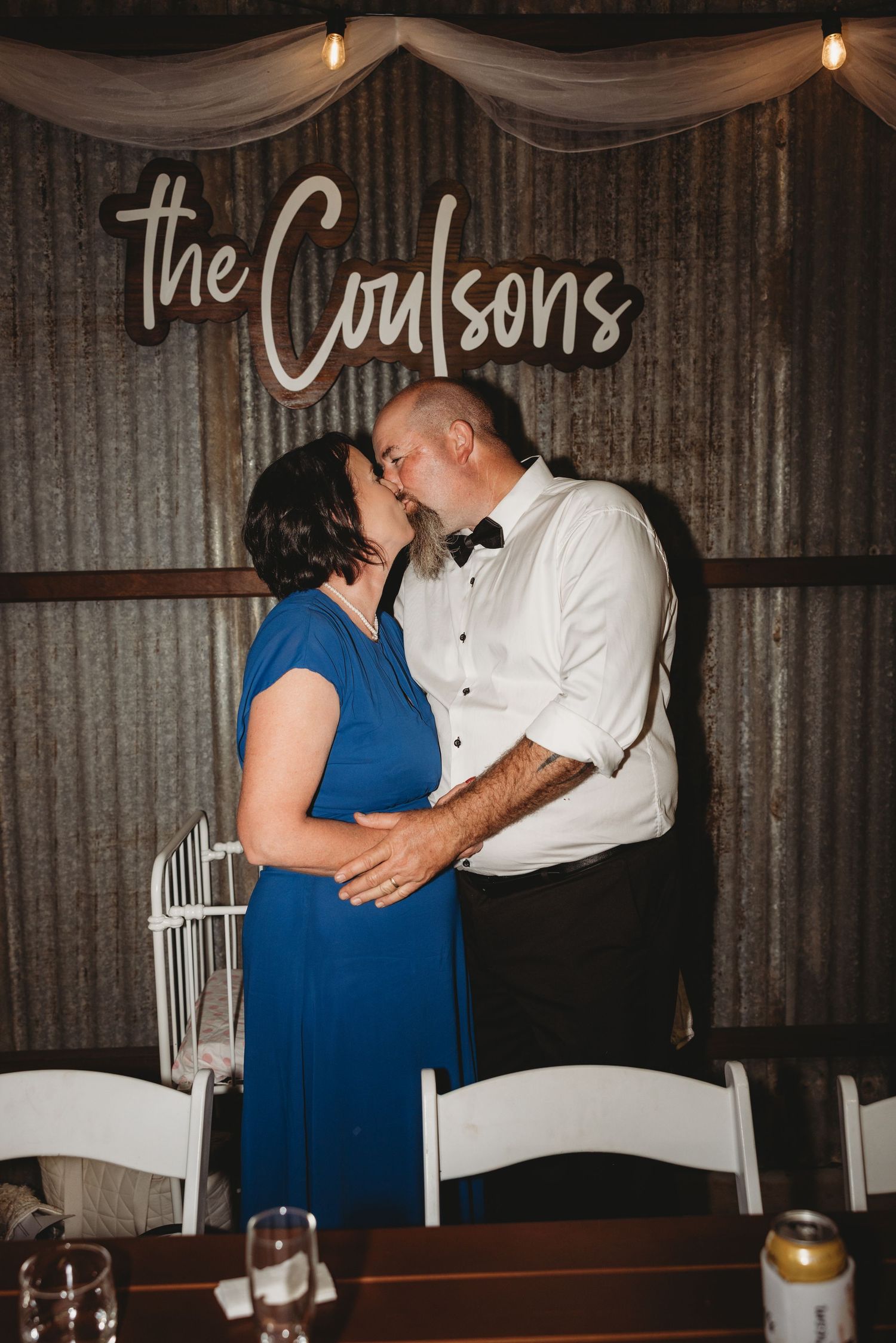 Wedding reception venue with rustic decor and couple sharing intimate moment under custom name sign.