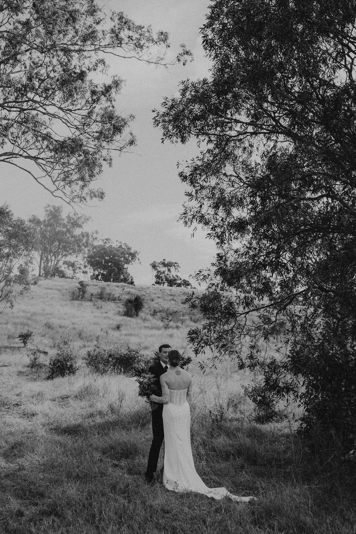 Black and white photo of bride and groom embracing in lush green hillside landscape.