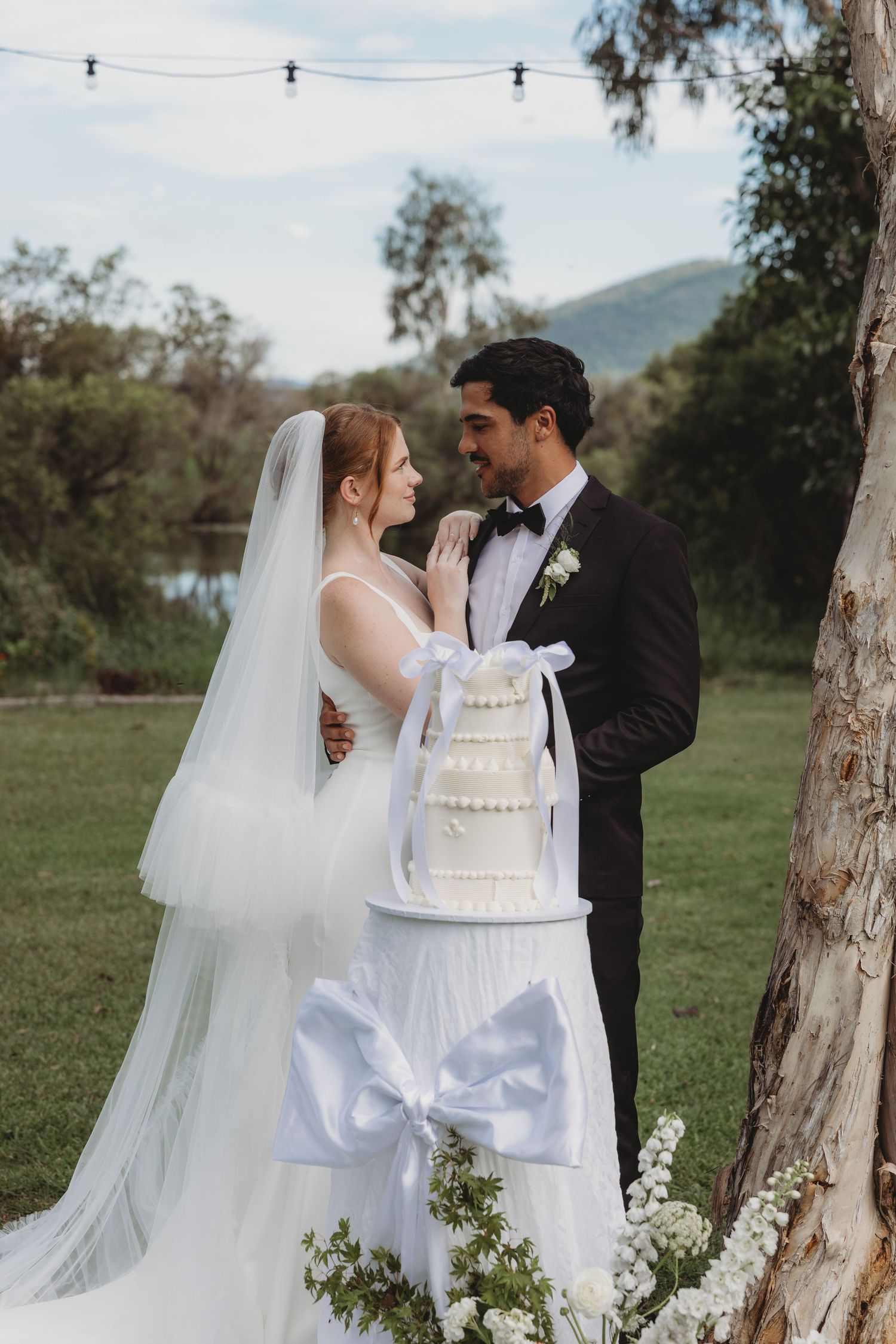 Elegant wedding cake display with white tiers against natural outdoor backdrop.