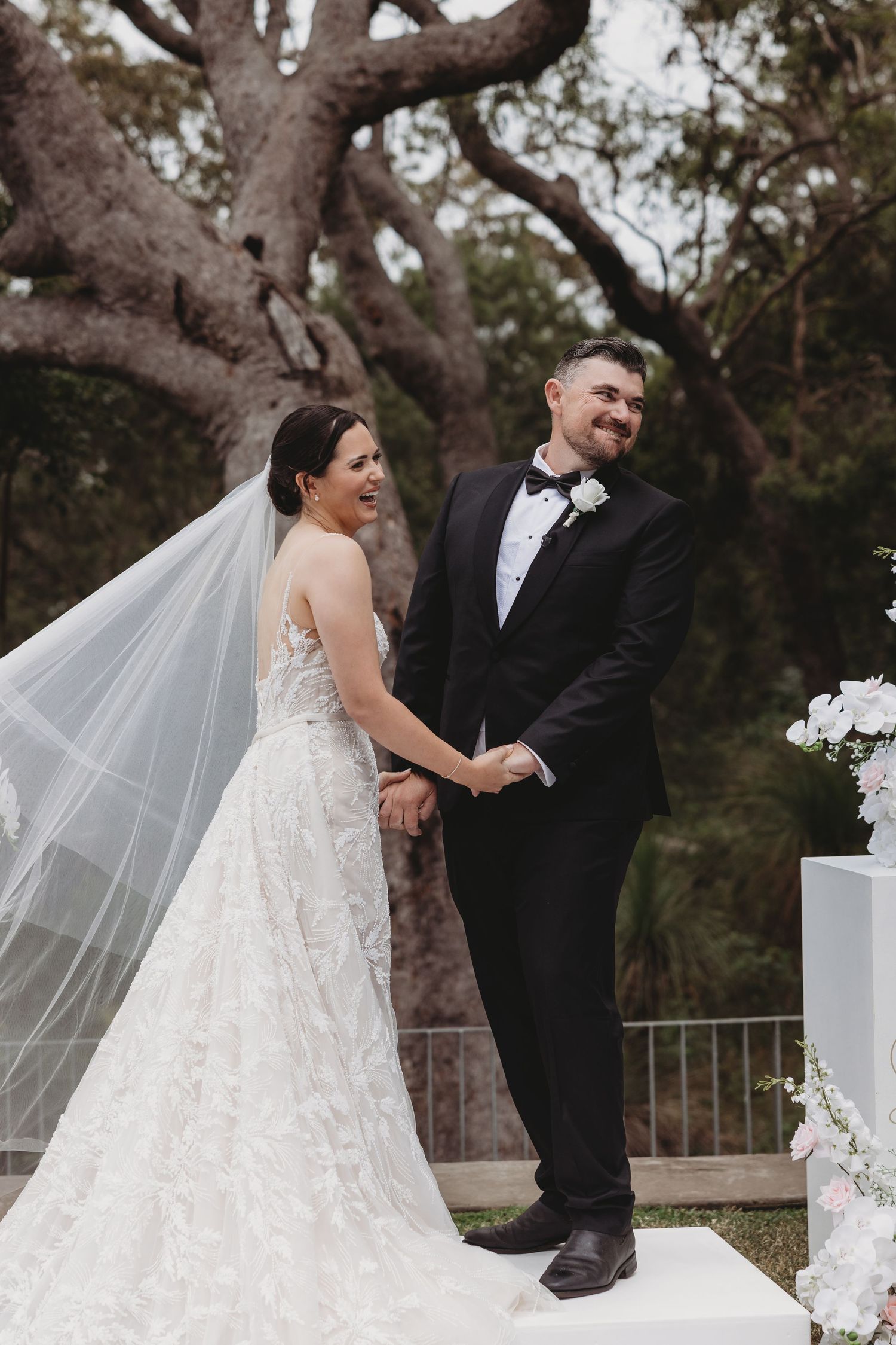 Wedding couple shares intimate moments in front of an outdoor ceremony backdrop with white florals.