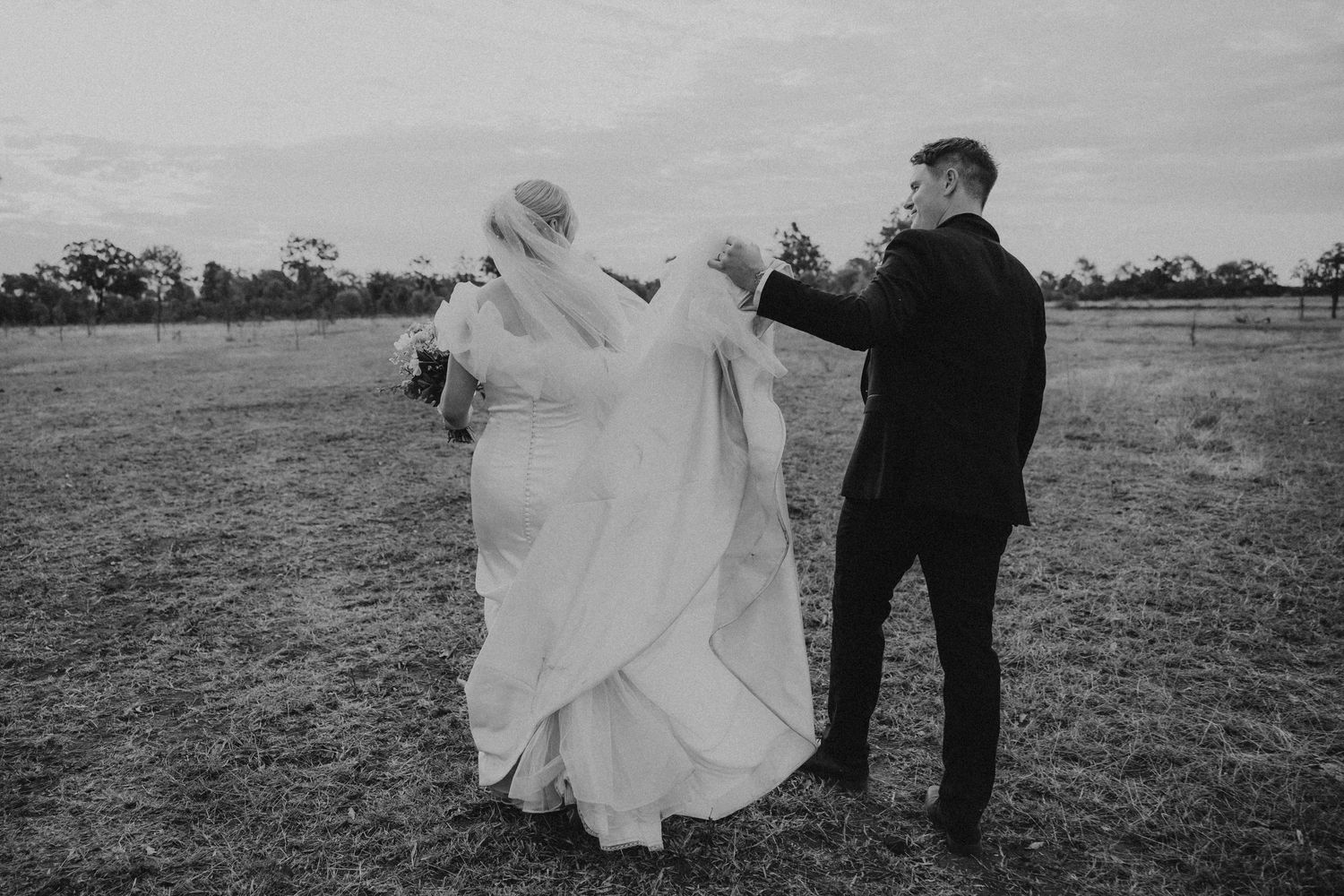 Romantic black and white wedding photos showing couple in field with dramatic lighting and flowing dress.