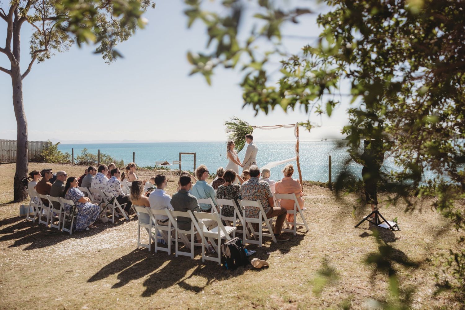 Panoramic shot of outdoor wedding venue with guests seated overlooking the water.