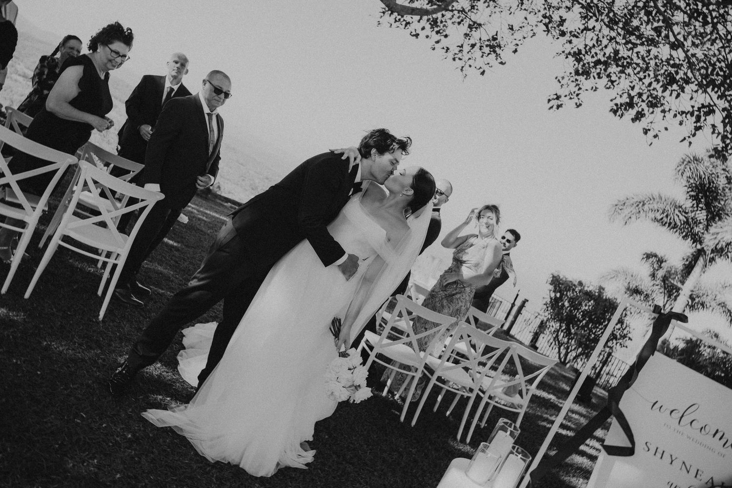 Wedding ceremony setup with white chairs on grass against mountain backdrop.