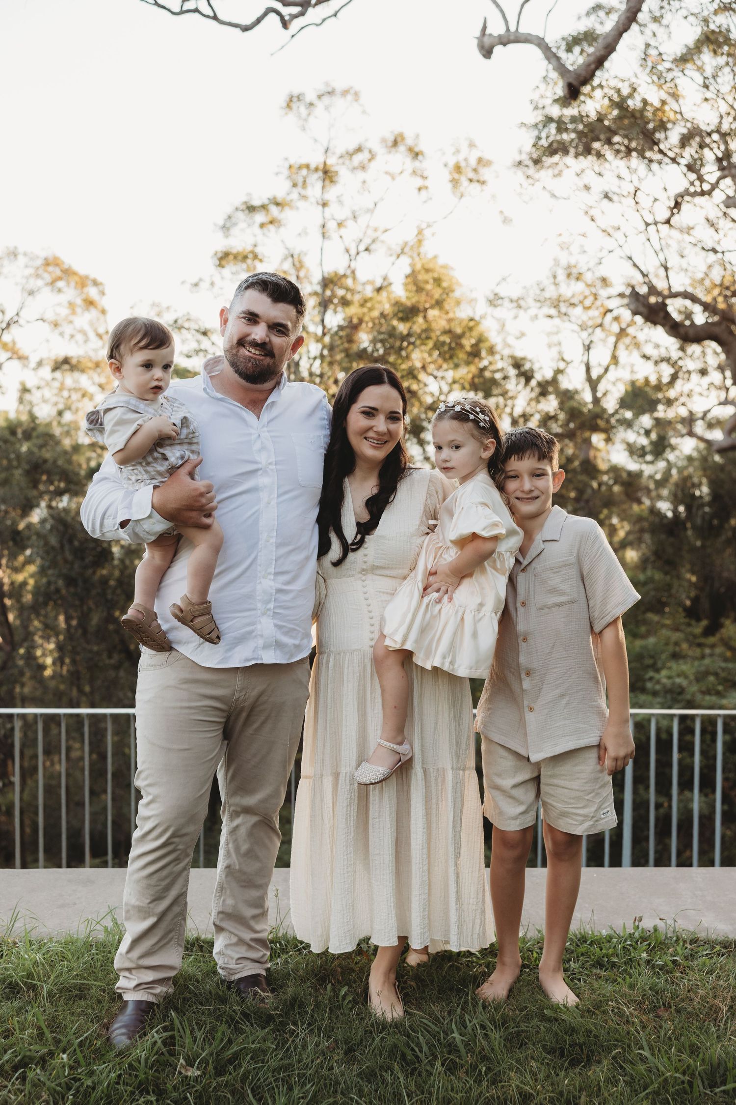Family gathered on grassy hill wearing matching neutral colored clothing.