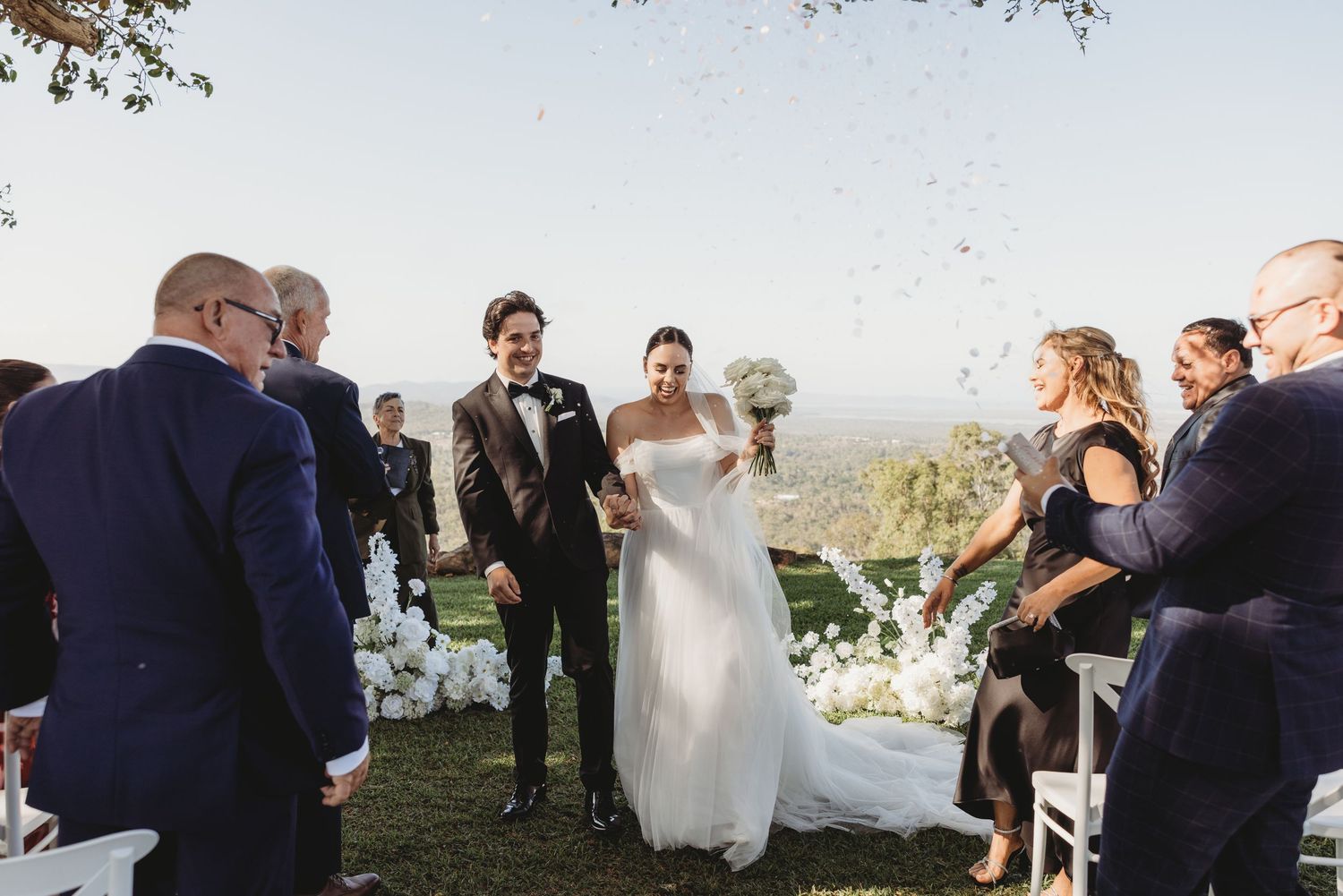 Wedding party and guests gather outdoors for celebrations with scenic natural backdrop.
