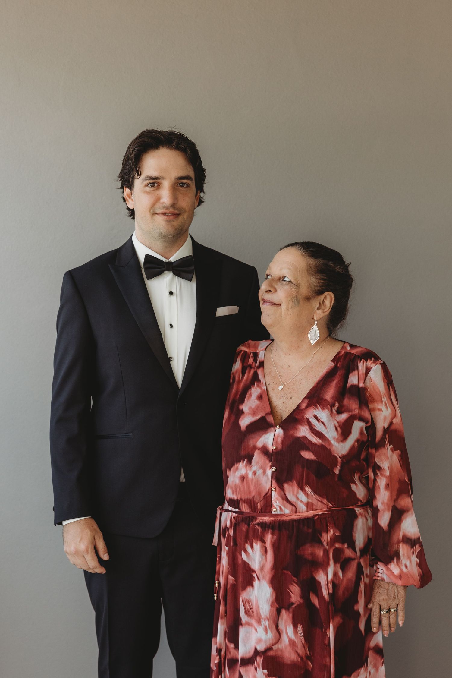 A formal portrait of two people, one in a tuxedo and one in a red patterned dress.