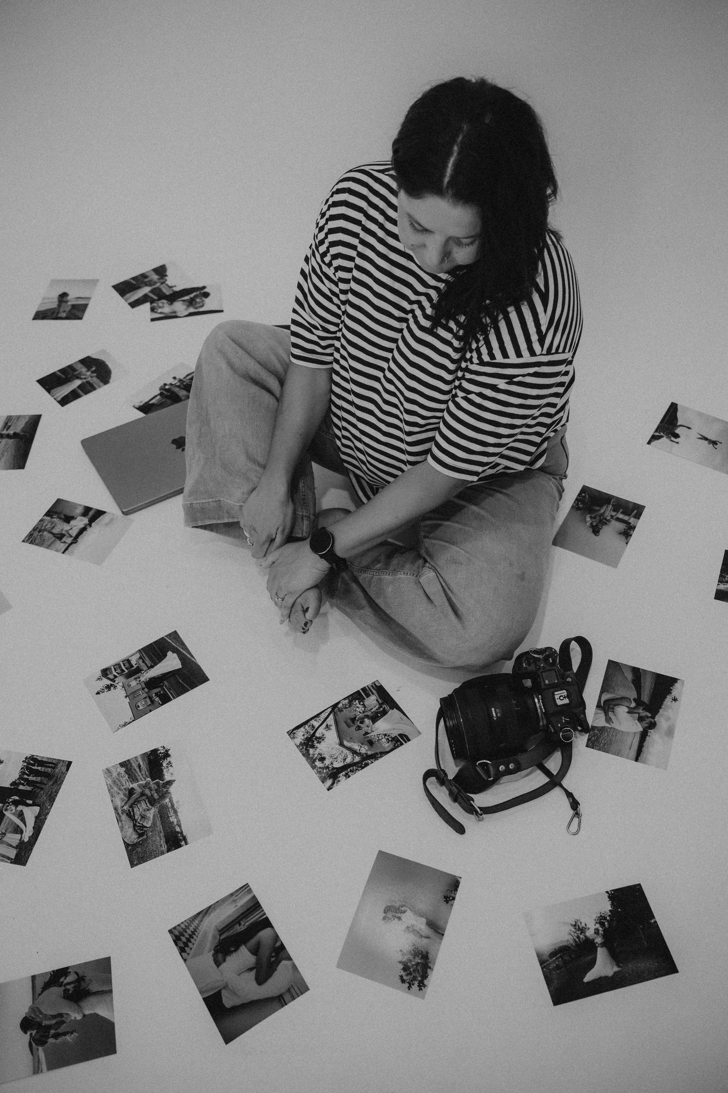 Person in striped shirt looking through scattered photographs on white surface.
