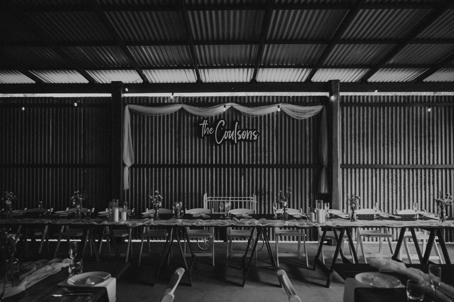 Industrial barn venue interior with corrugated metal walls and hanging string lights.