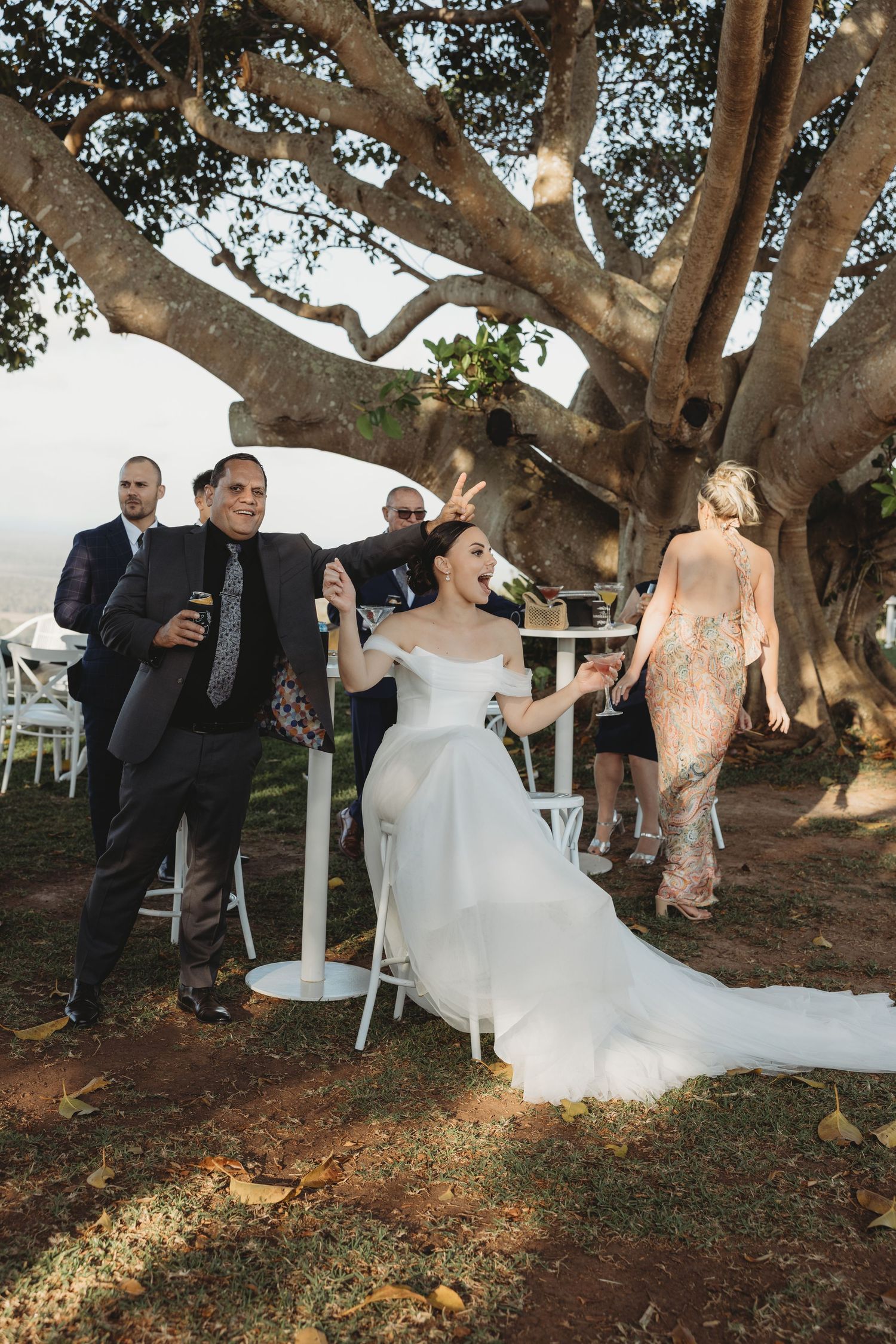 Guests mingle under sprawling tree branches at an elegant outdoor wedding reception.