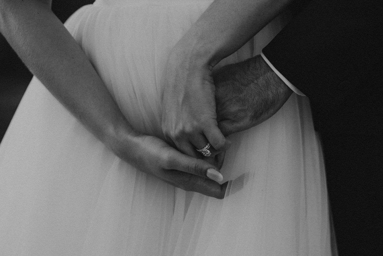 Close-up detail of hands holding white wedding dress fabric.