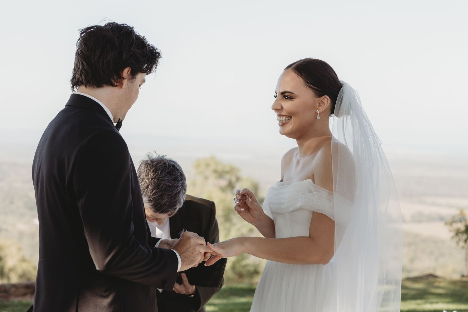 A romantic wedding moment captured at sunset with a flowing white veil against a scenic hilltop backdrop.