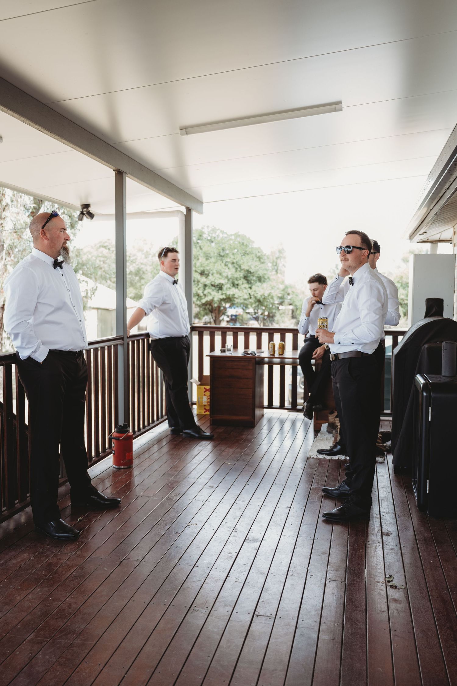 Wedding party members in formal attire gather on a wooden deck during preparations.
