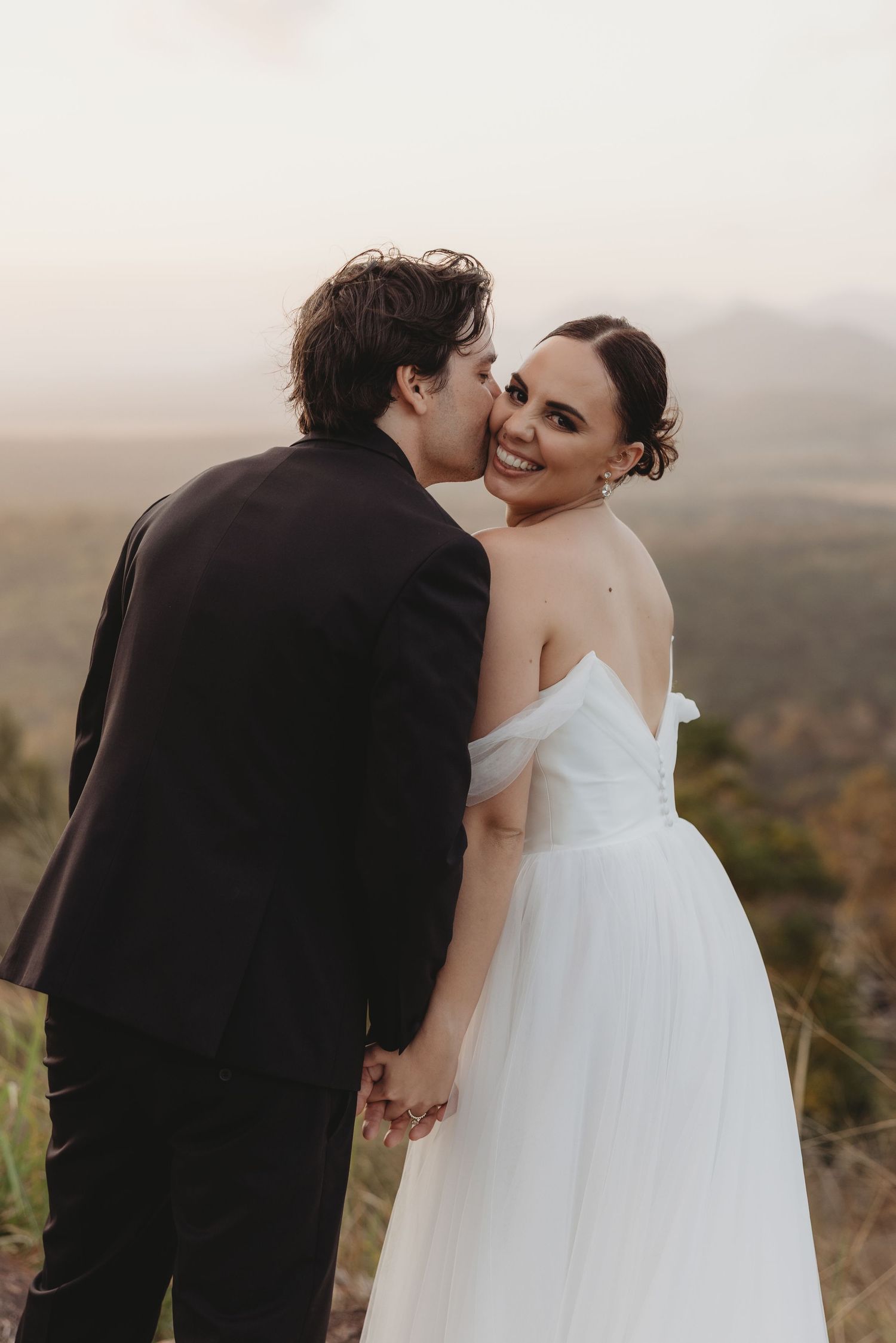 Intimate wedding moment shared between couple on hilltop during sunset.