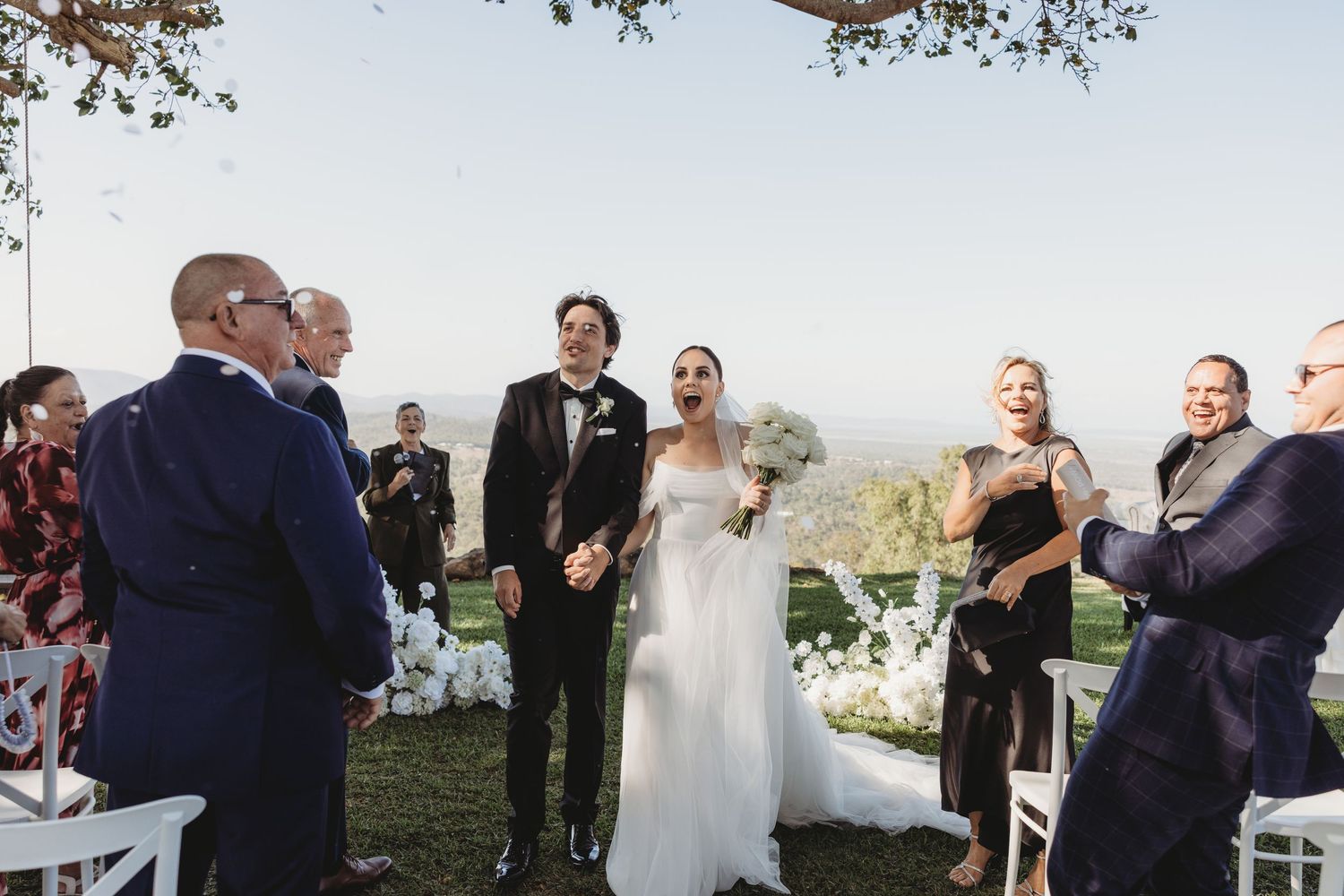 Wedding ceremony setup outdoors with white chairs and natural scenery in the background.