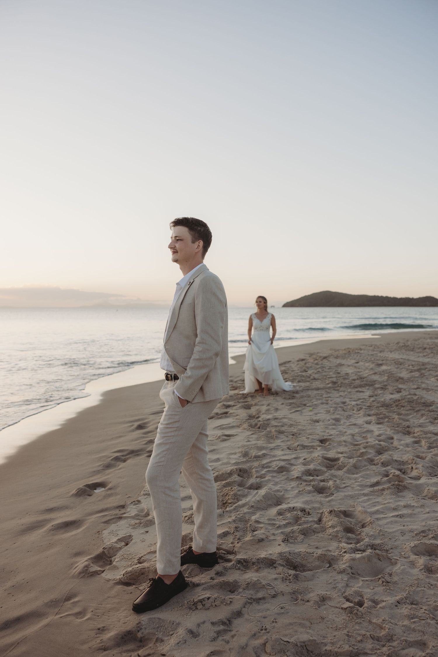 Two people enjoy a romantic moment on a serene beach with distant islands visible on the horizon.