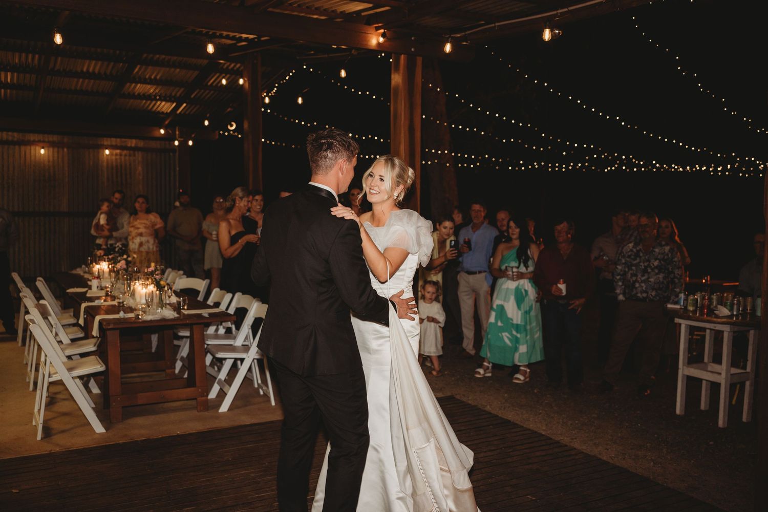 Couple sharing their first dance at a rustic wedding reception under string lights.