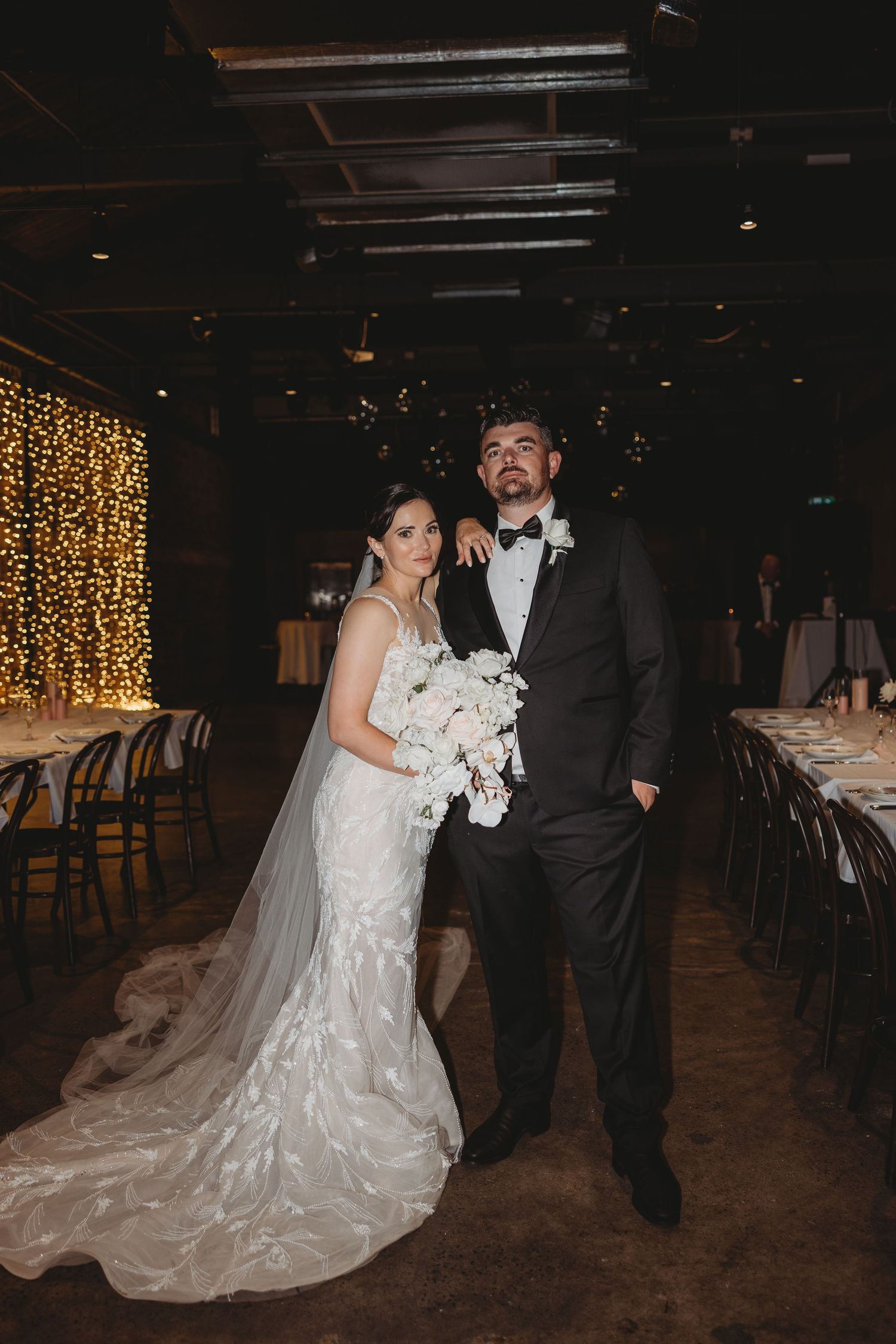 Wedding couple dances in reception venue with fairy lights and long train dress.