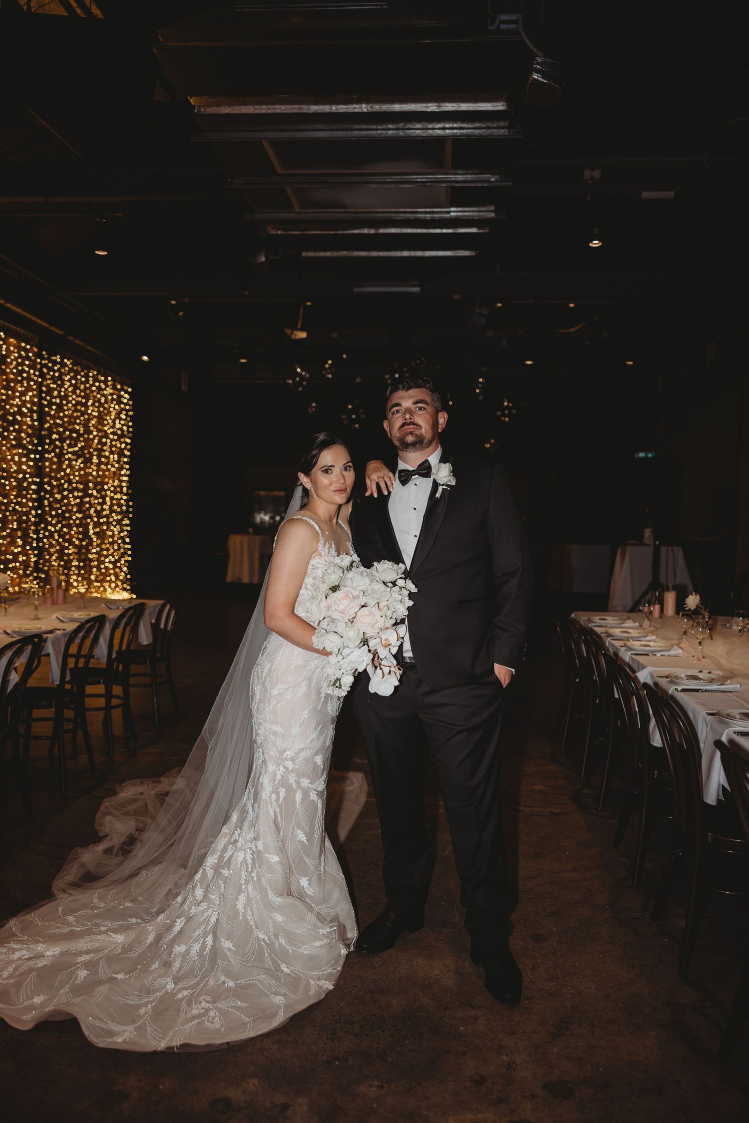Wedding couple dances in a romantic reception venue with fairy lights in the background.