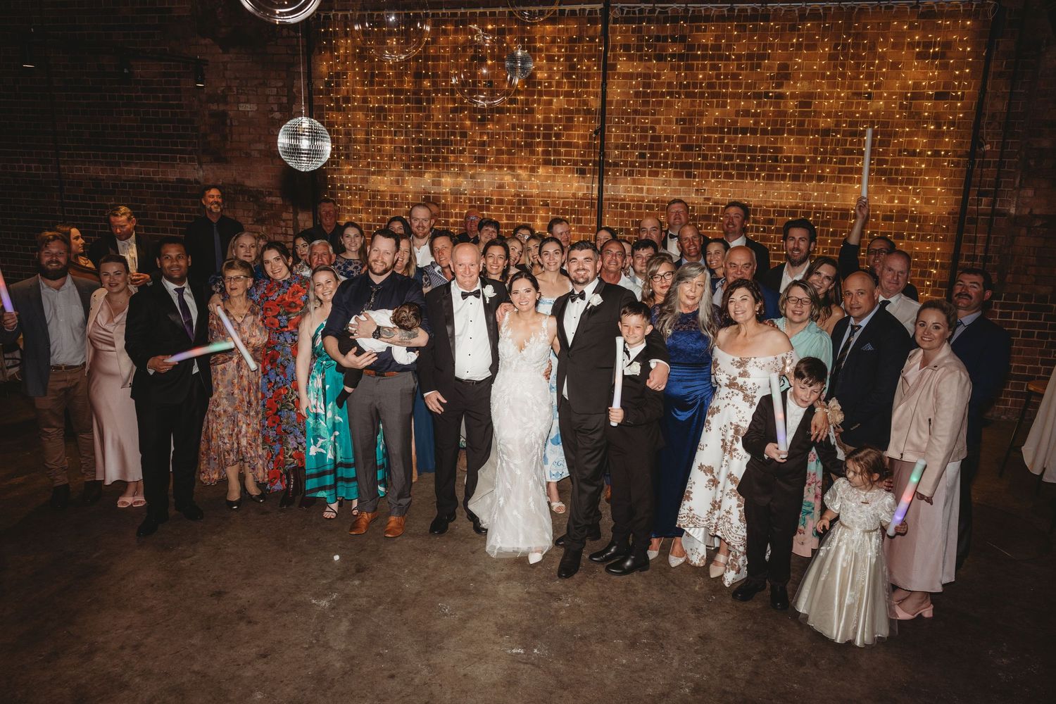 Wedding reception party with guests dancing under disco ball and string lights.