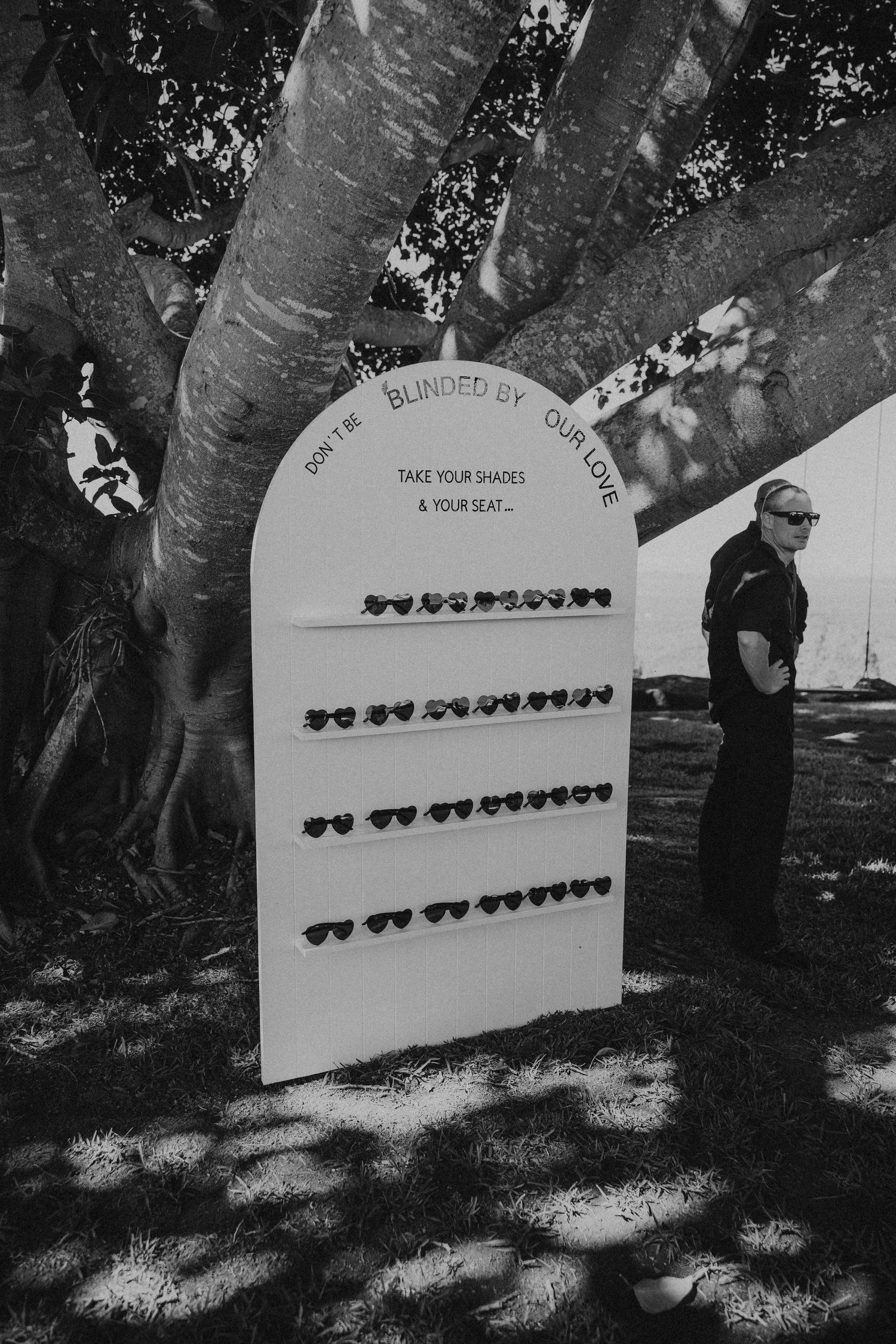 A black and white photo series showing a wedding seating chart board displayed outdoors under trees.
