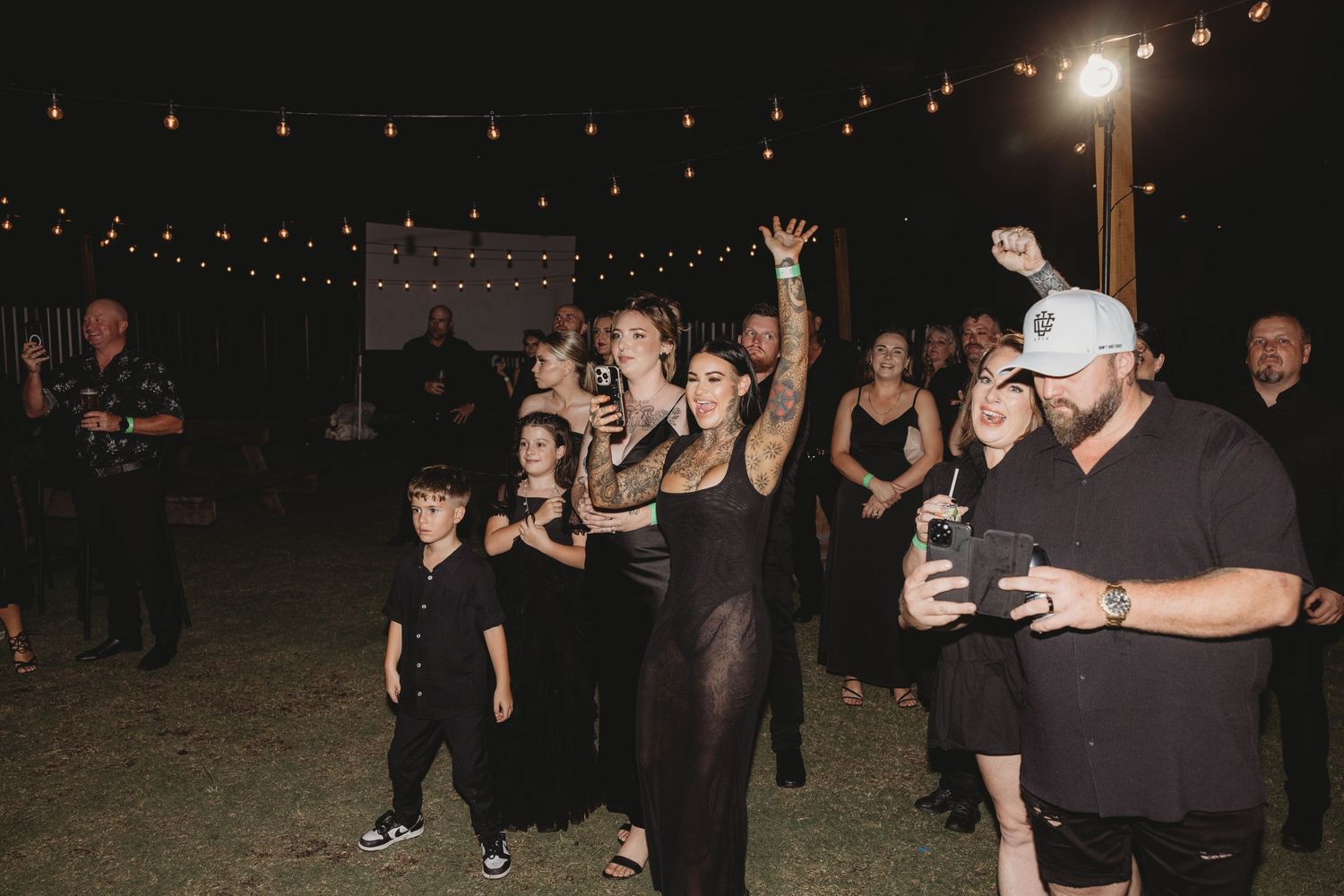 Wedding reception guests dancing under string lights at night.