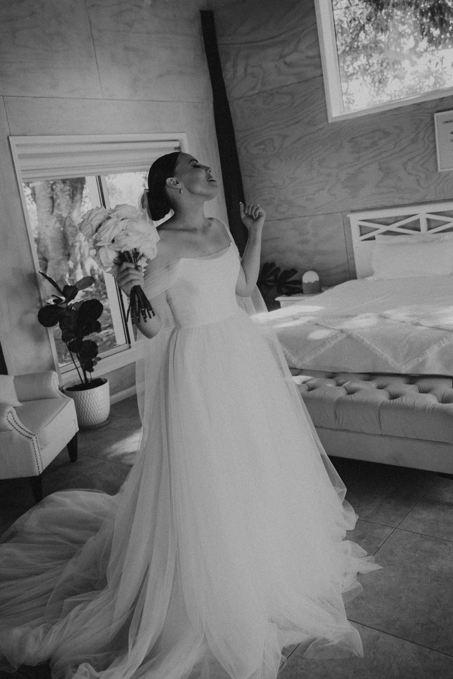 Bride in flowing white gown poses in rustic getting ready room with vintage decor.