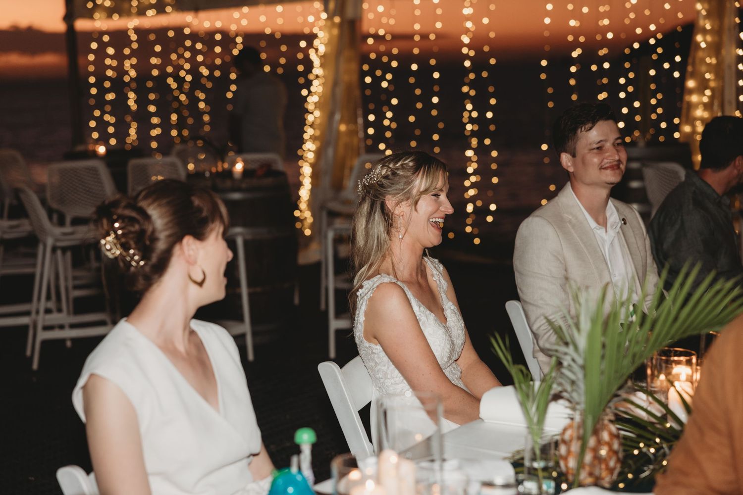 Wedding reception tables decorated with string lights and white linens in an outdoor tent setting.