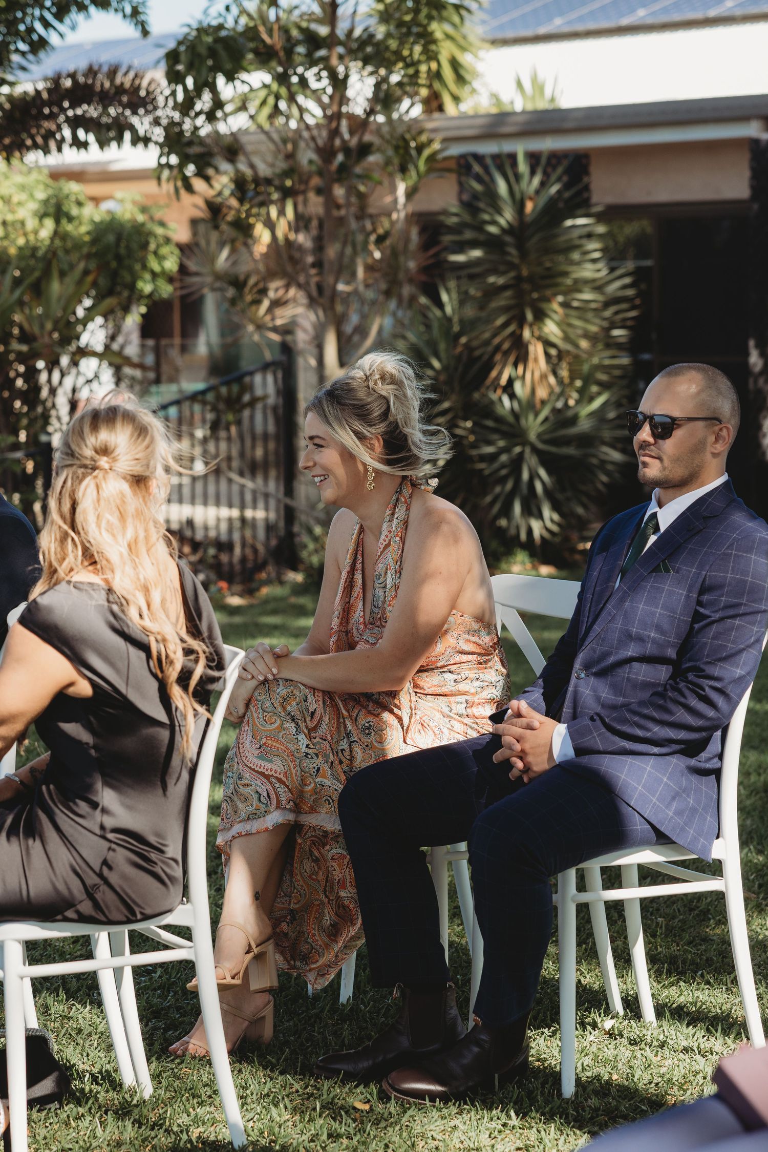 Wedding guests relaxing in white chairs on a grassy lawn during a sunny outdoor celebration.