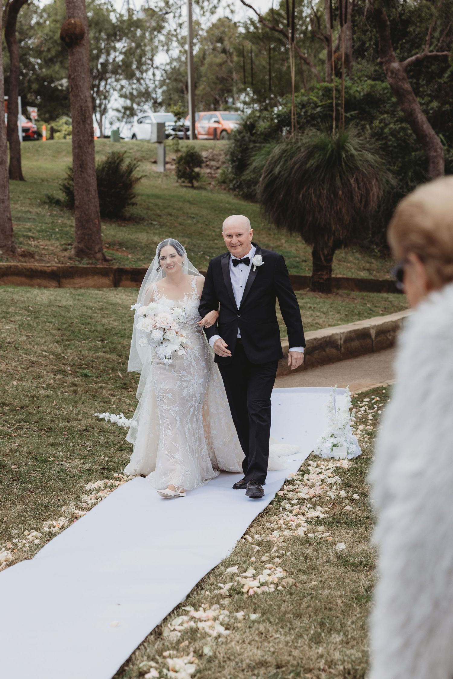 Couple walking down a white aisle runner in an outdoor garden setting during their wedding ceremony.