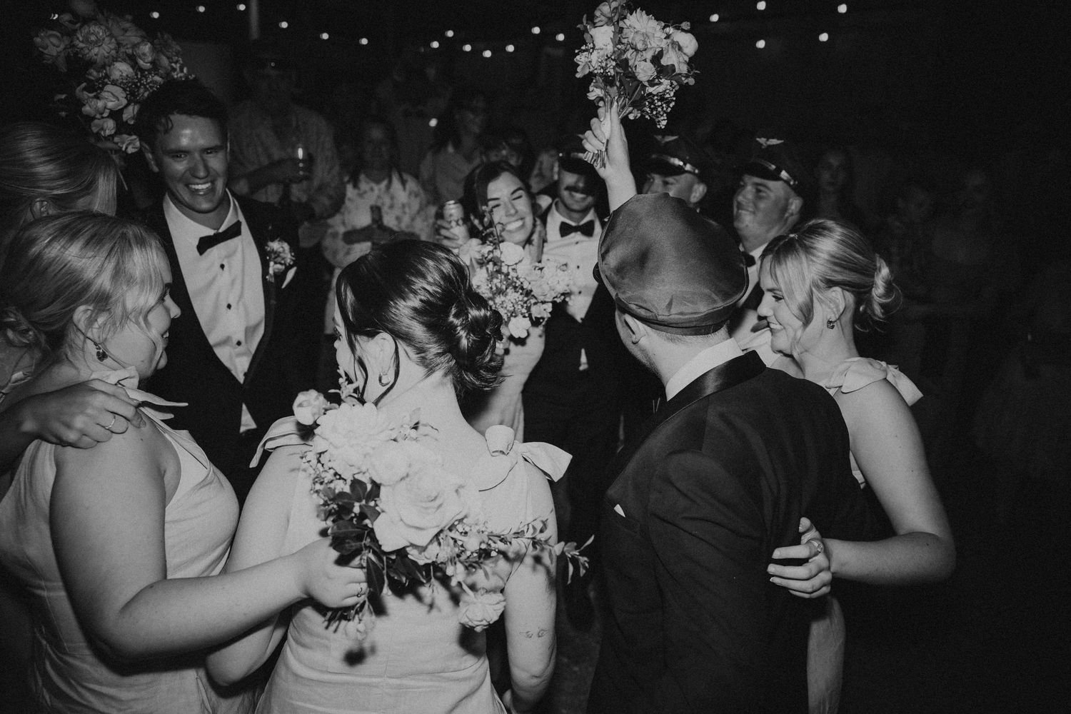 Black and white photo of wedding guests dancing and celebrating at night.
