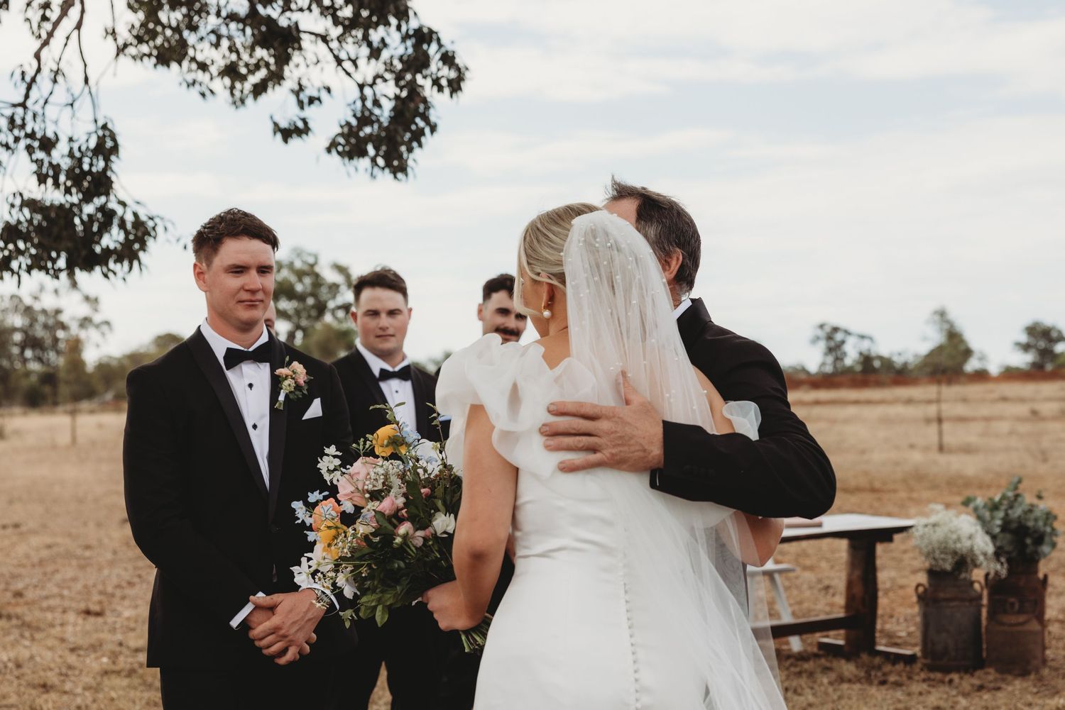 Emotional moments captured during a countryside wedding ceremony near a large tree.