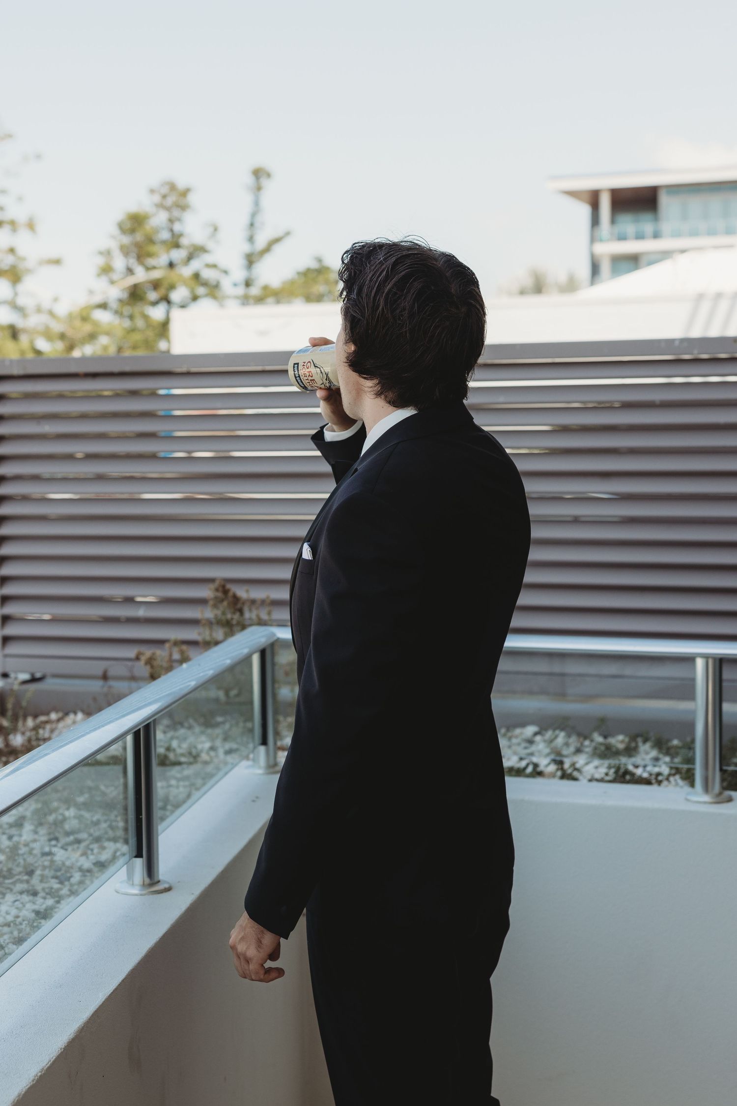 Person in formal wear looking out over a modern balcony railing.
