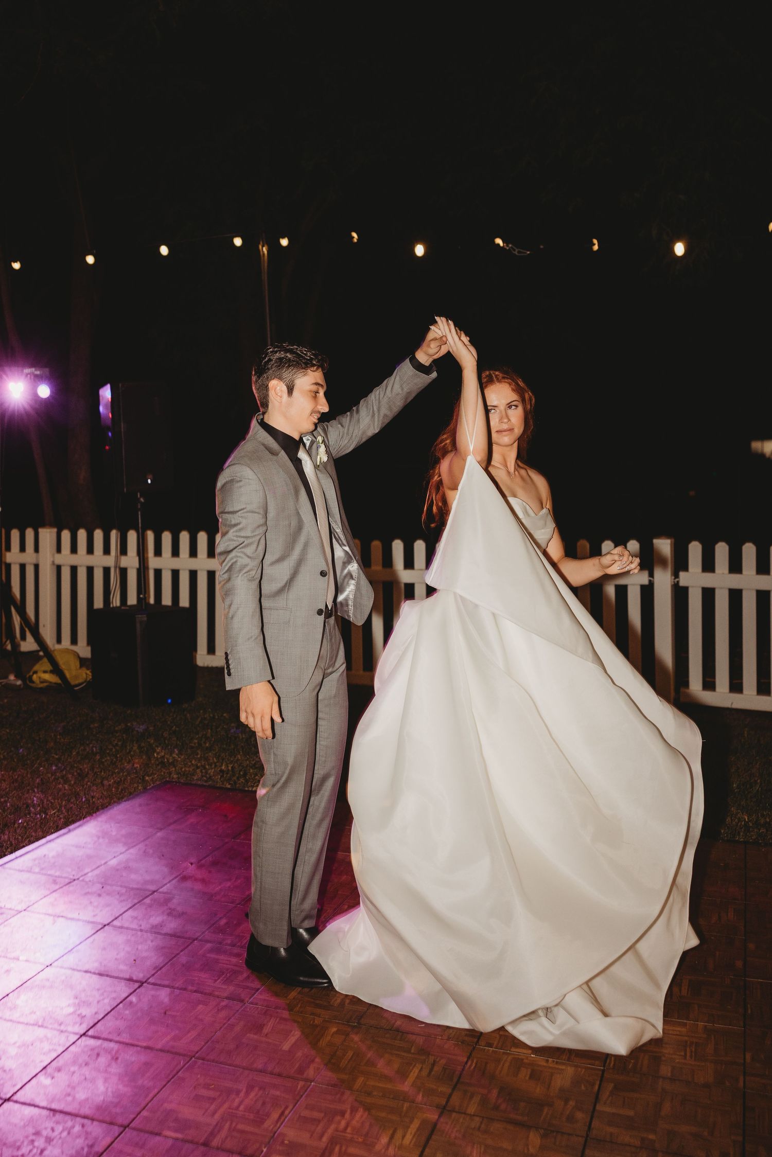 Couple performing their first dance on an illuminated outdoor dance floor at night.