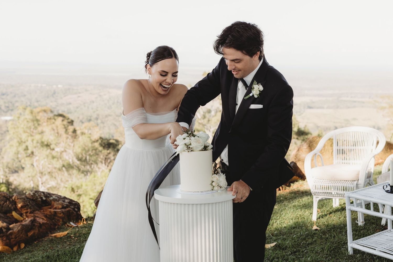 Candid moment of newlyweds sharing cake at their outdoor hilltop wedding reception.