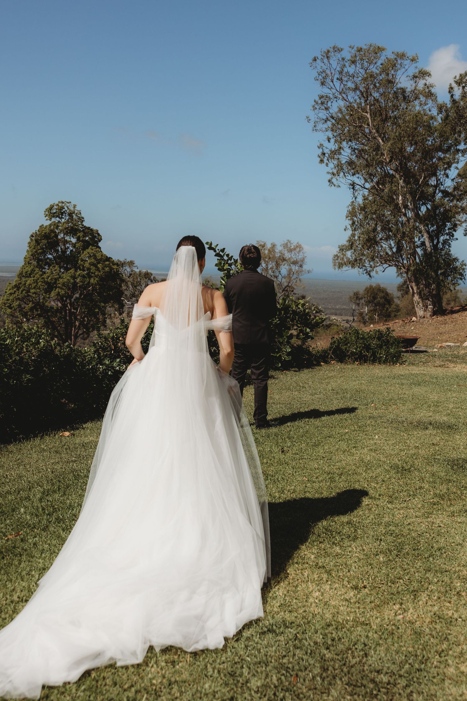 Outdoor wedding photos on a grassy hillside under blue skies with eucalyptus trees.