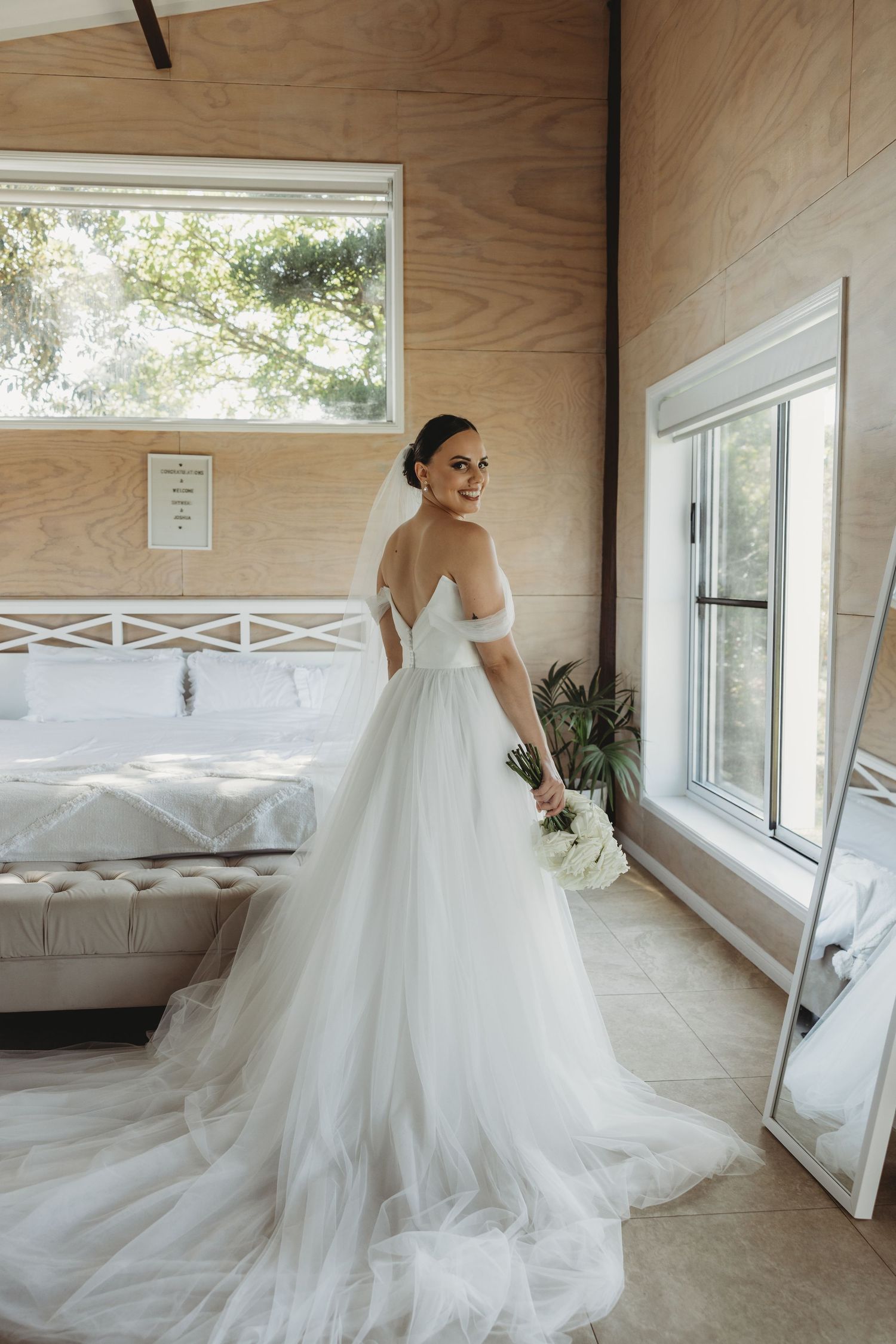 Elegant bridal gown with tulle skirt and long train photographed in a rustic room with windows.