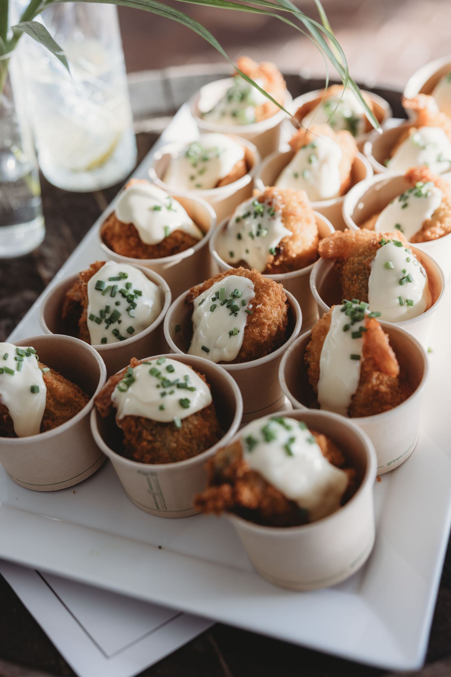 Appetizer plates of breaded shrimp with white sauce and herbs served in small ceramic cups.