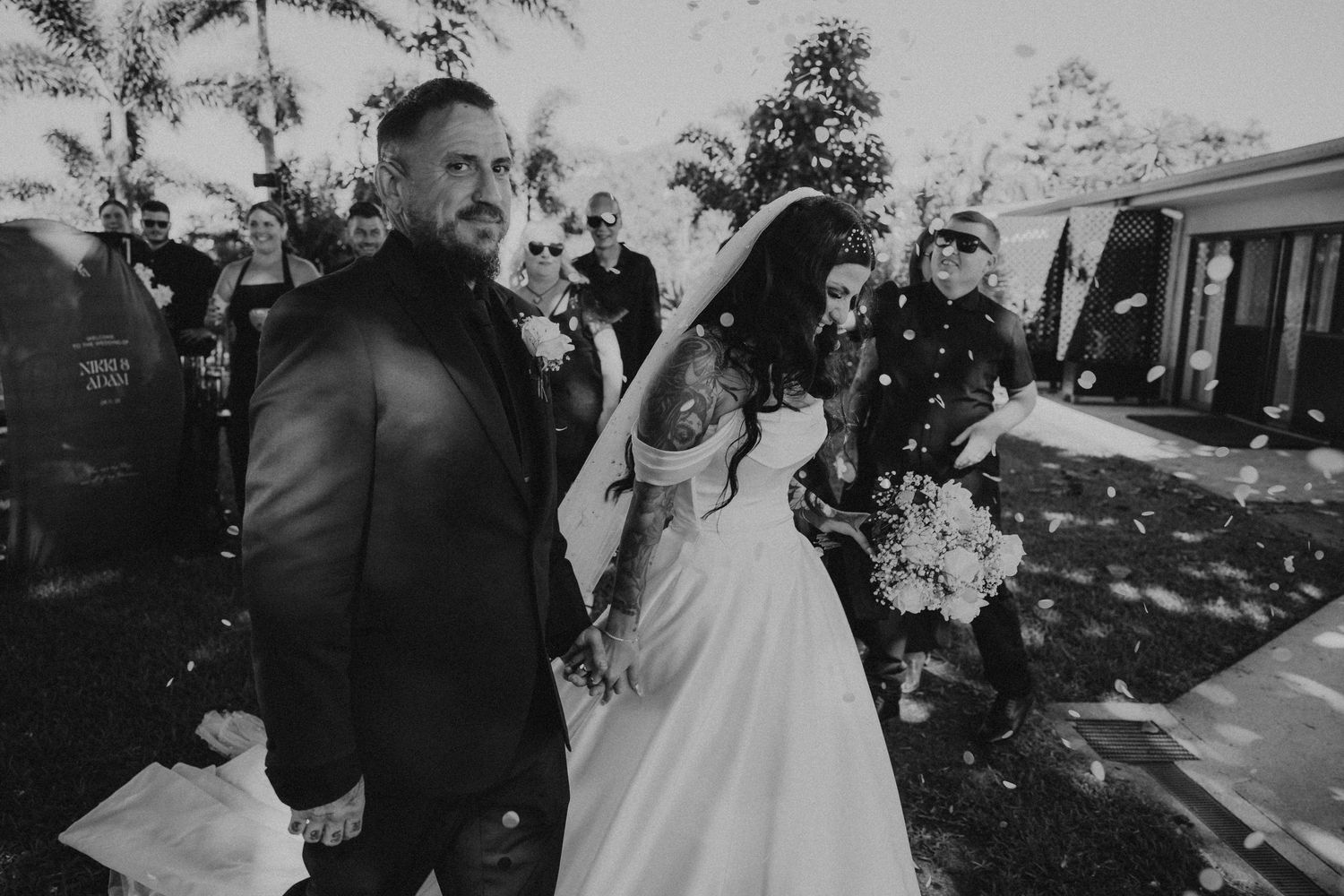 A couple celebrates their wedding day outdoors with guests throwing flower petals during the recessional.