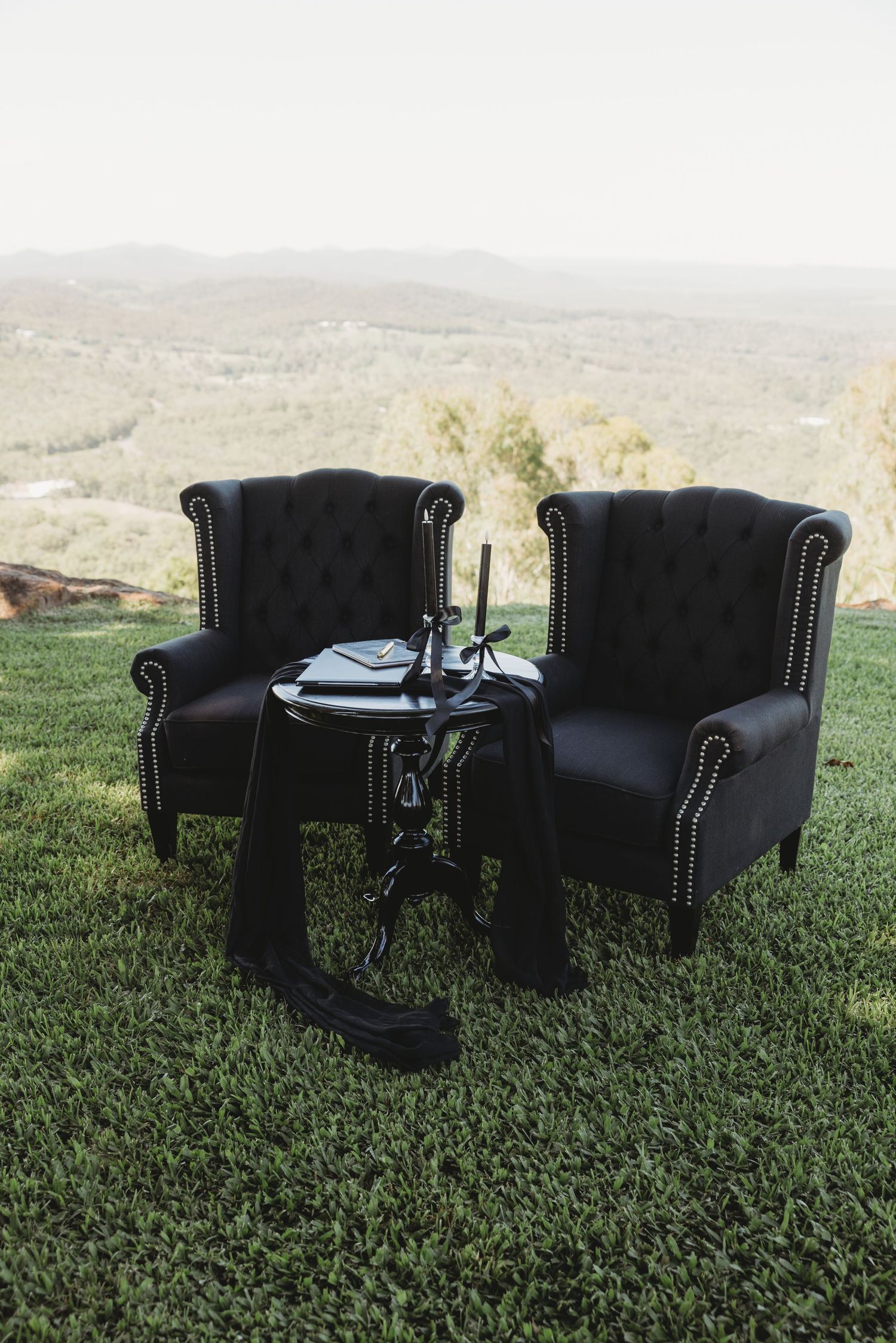 Black leather armchairs arranged on green grass with scenic mountain views in the background.