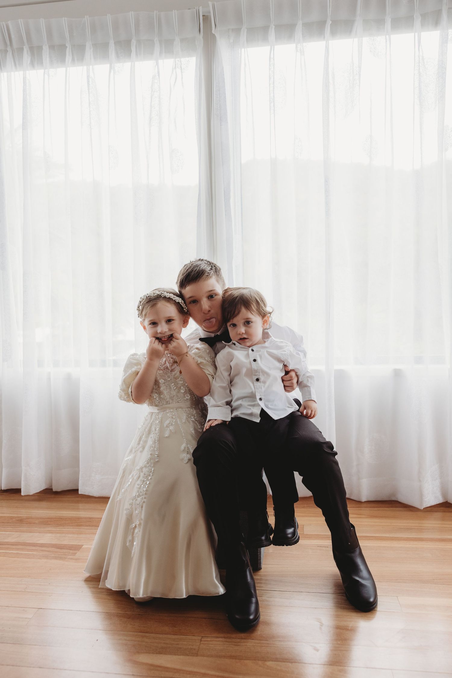 A sweet family moment captured in front of white curtains on hardwood floors during a formal occasion.