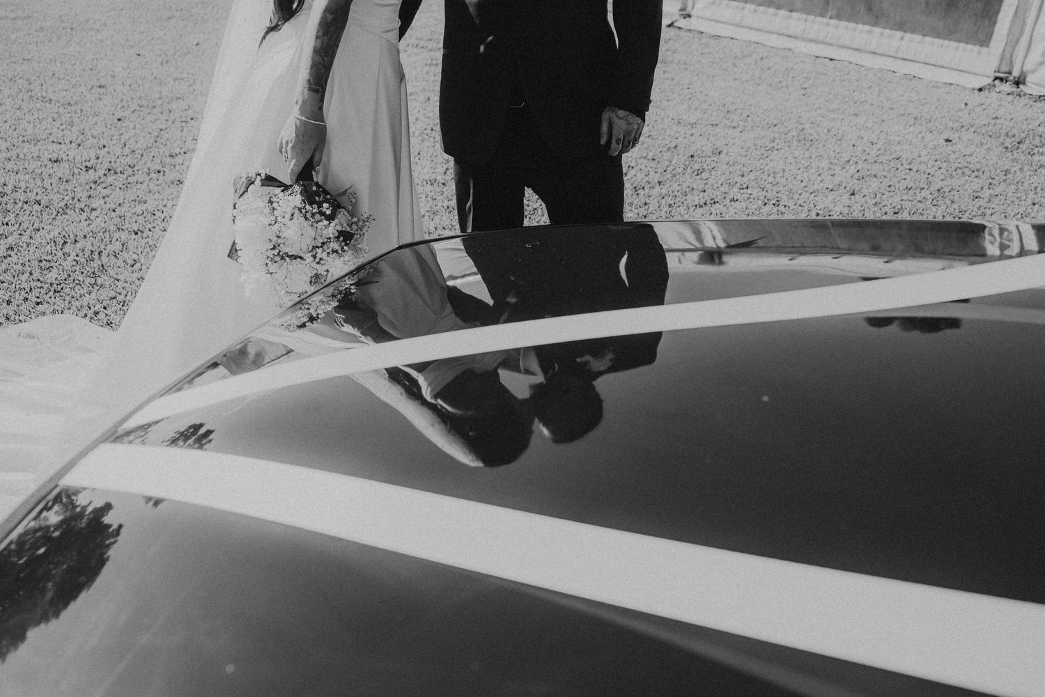 Artistic black and white reflection of wedding couple in car window.