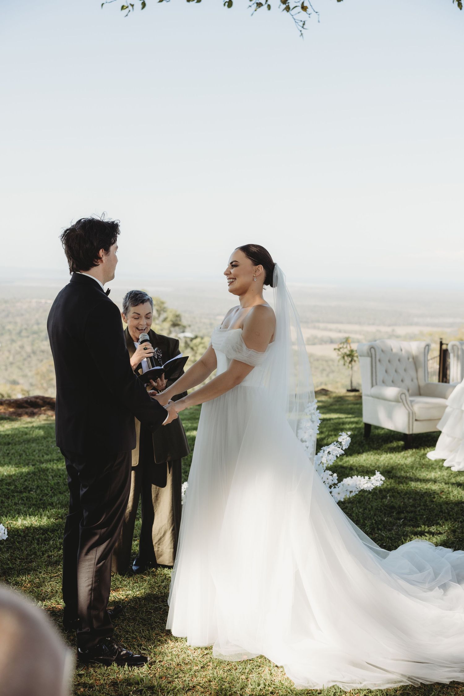 Intimate outdoor wedding ceremony taking place under tree branches with scenic valley views.