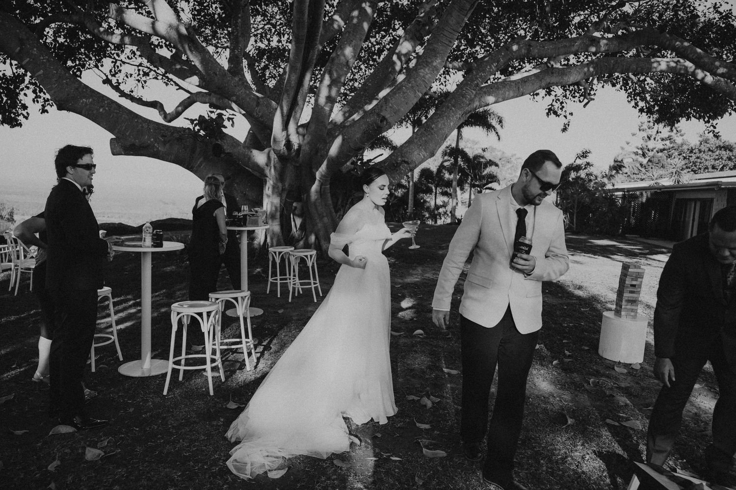 Black and white photos of guests mingling under large trees at an outdoor event.