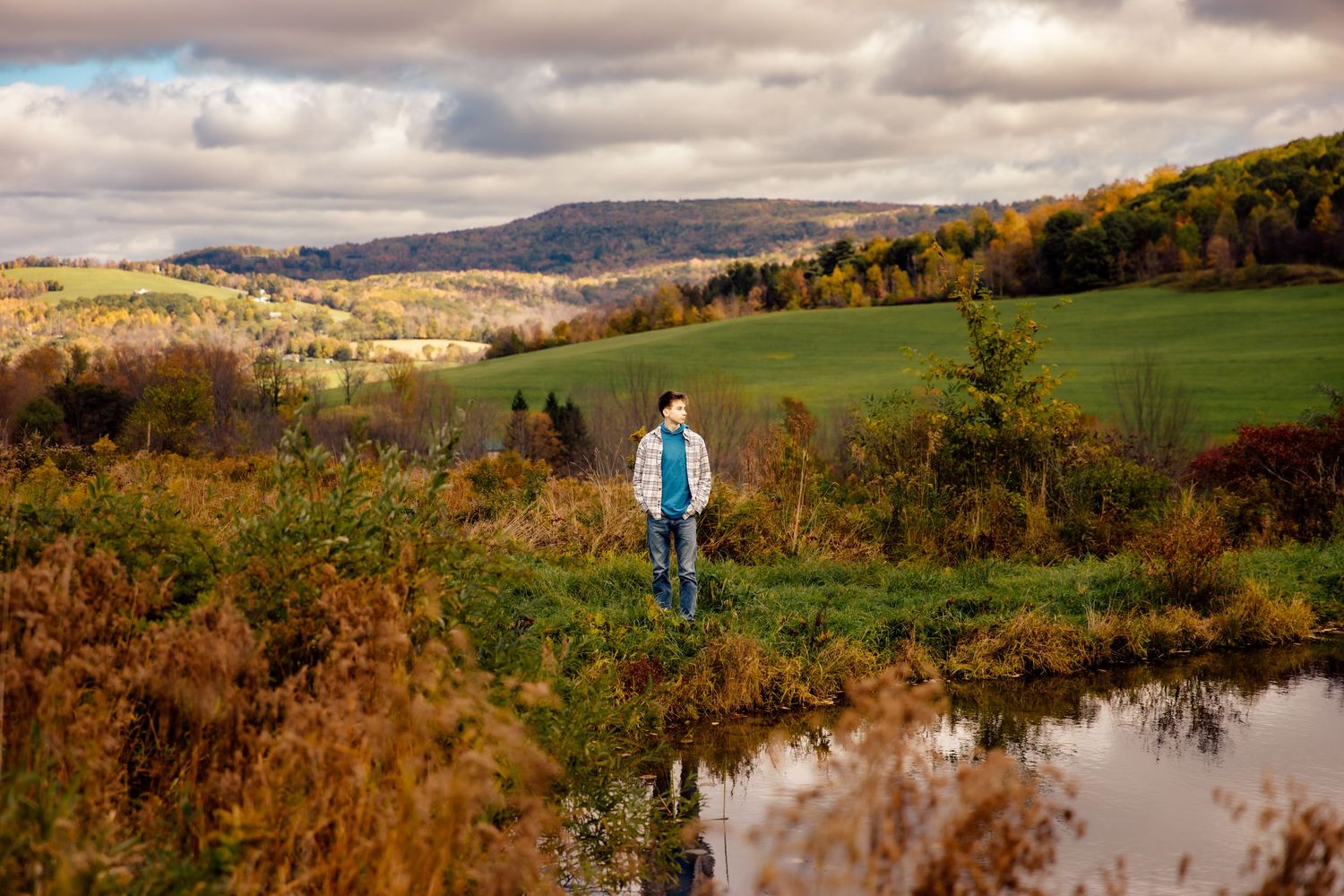 Boy standing next to pond with mountain view in the background