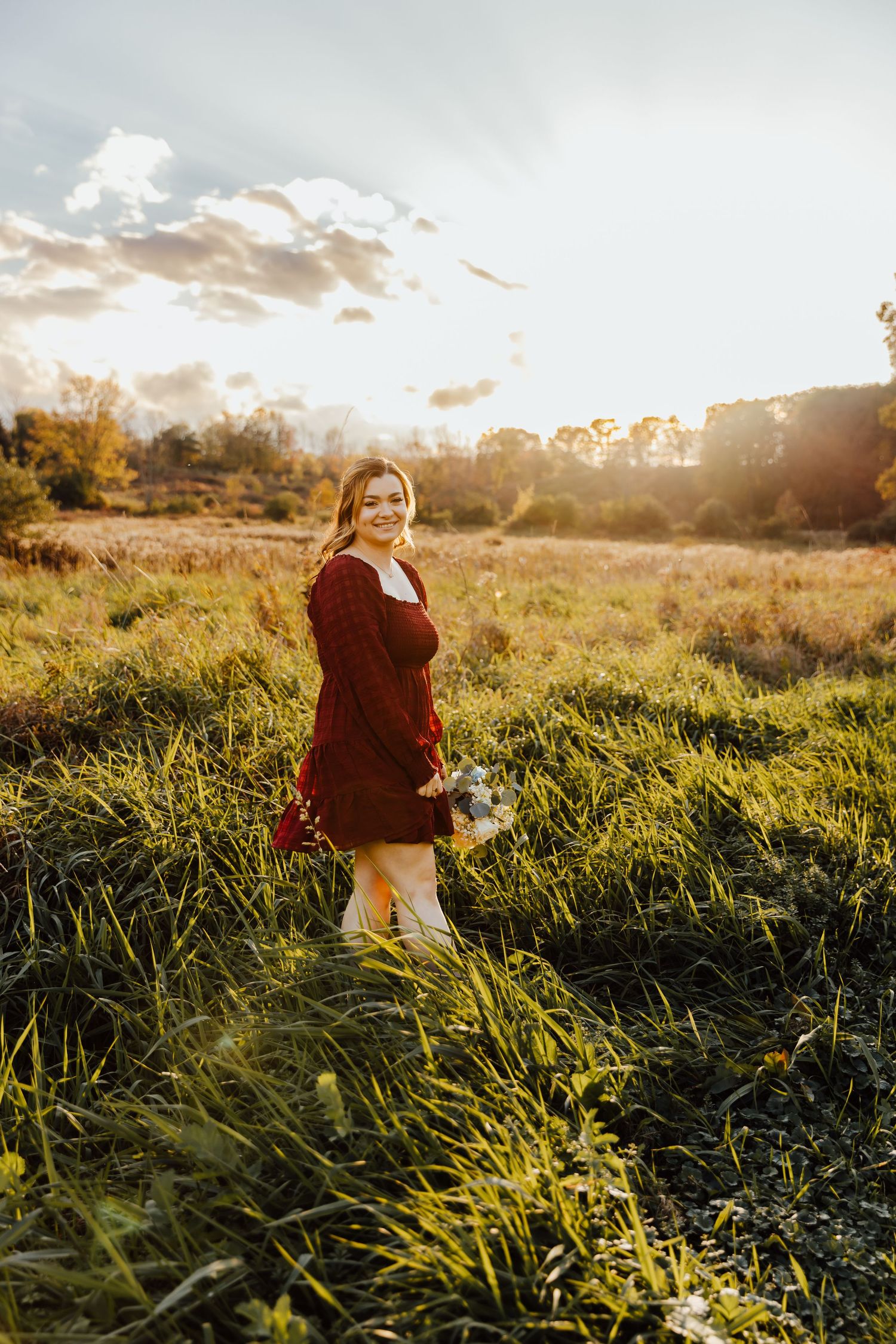 Girl wearing maroon dress posing in field in golden hour light